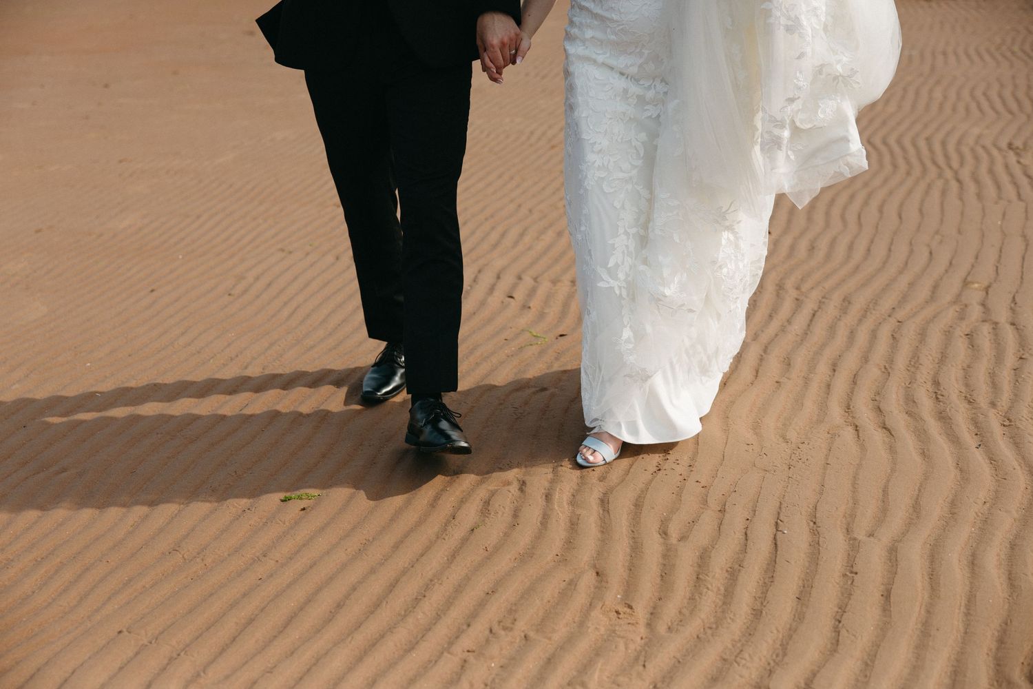 Wedding couple's silhouettes against textured sand patterns on beach.