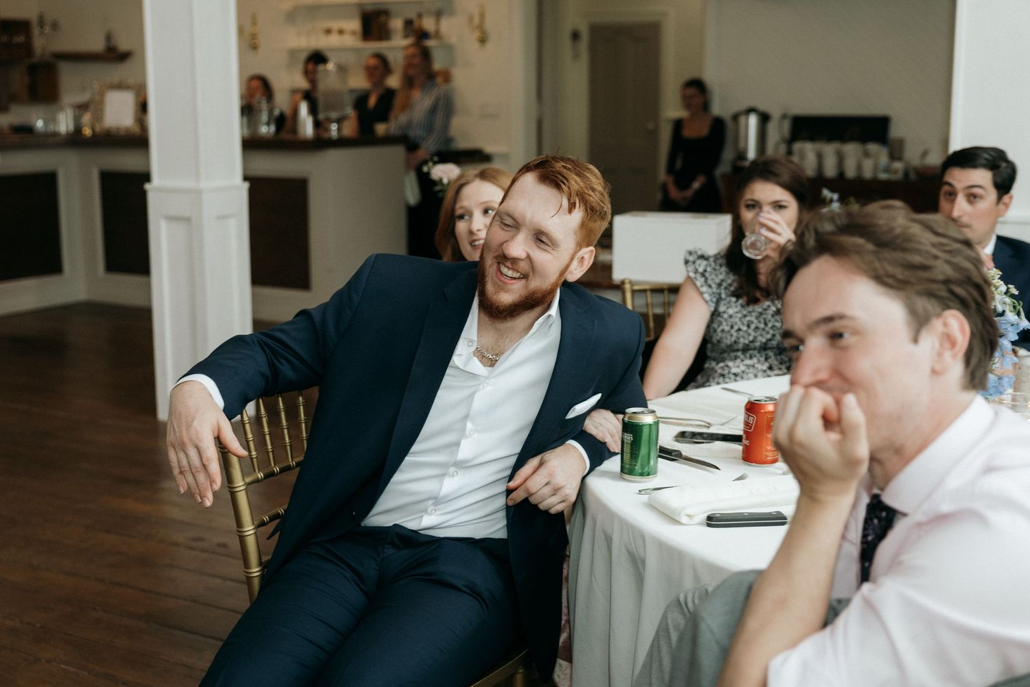 Wedding guests share laughs during reception speeches at decorated venue.