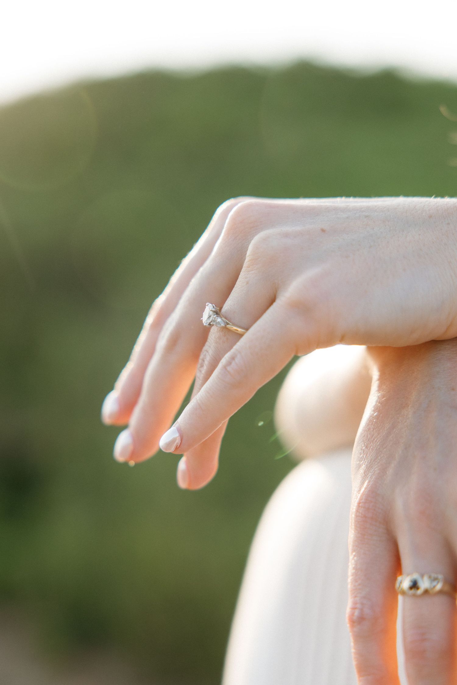 Close-up of womans hand displaying diamond engagement ring resting on mans hand outdoors.