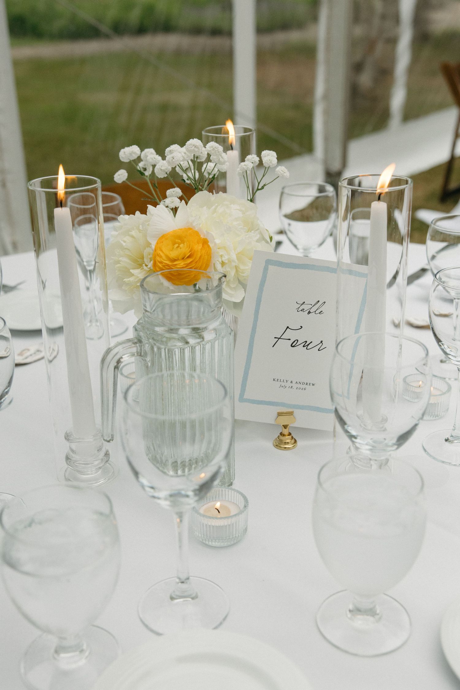 Elegant wedding table setting with white flowers, yellow ranunculus, and candles.
