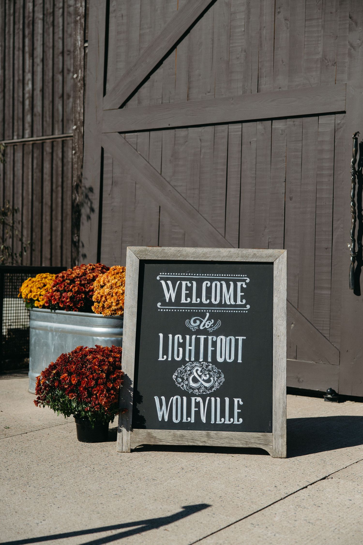 Welcome signs with text displayed against a dark wall with orange mums.