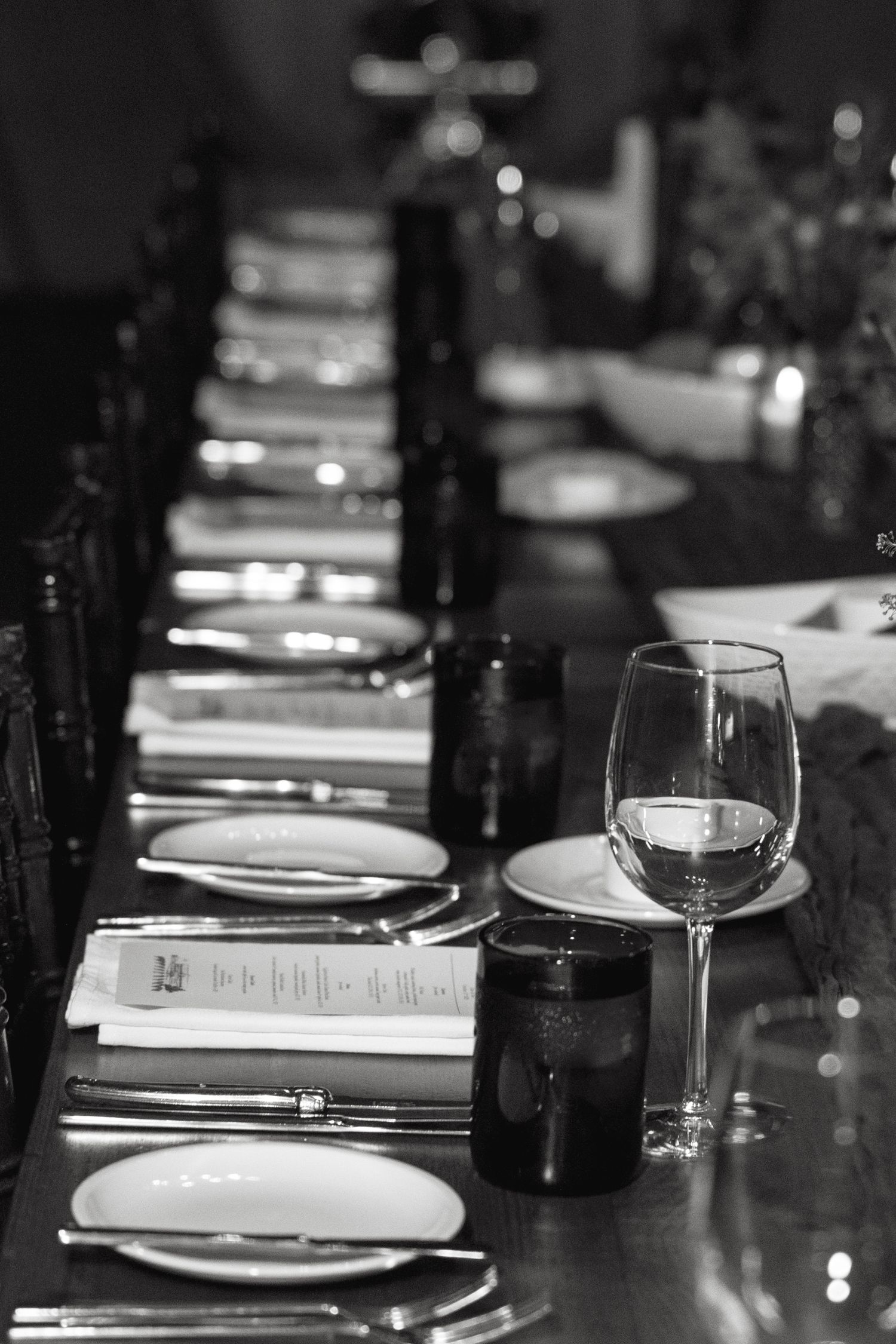 Black and white photo of formal dining table settings with wine glasses and plates.