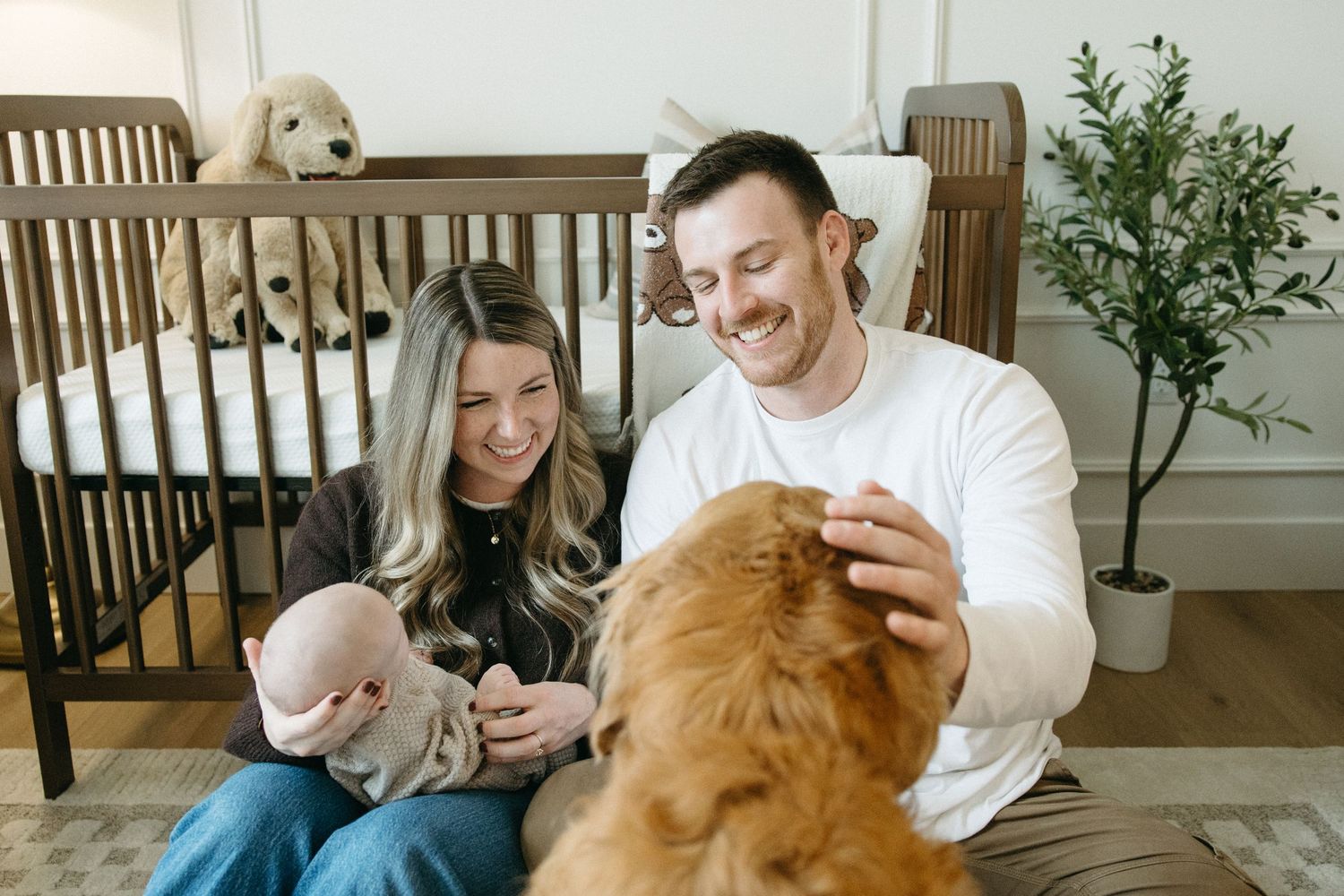 Family relaxing in nursery with golden retriever and baby.
