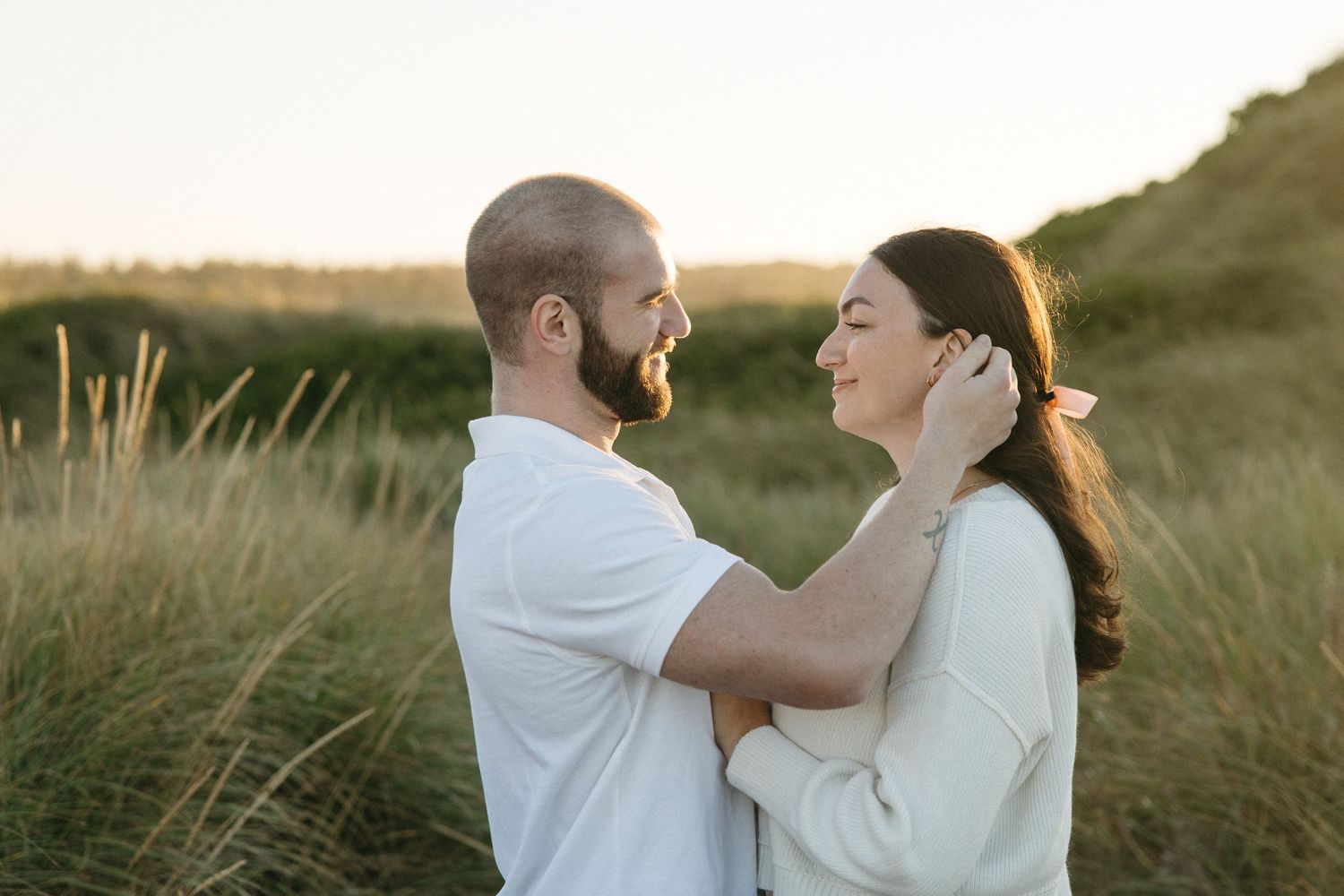 Couple holding each other close in evening sunlight on coastal dunes.