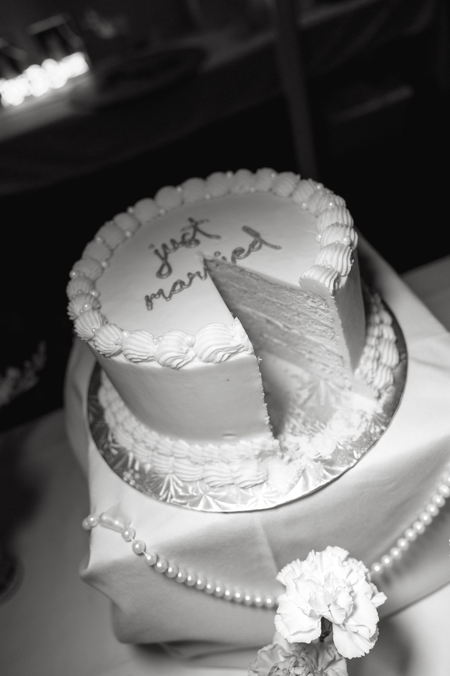 Two-tier white wedding cake inscribed with just married on a decorated table in black and white.