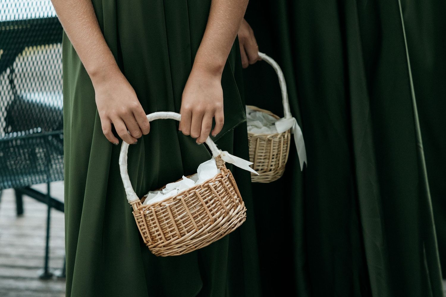 Flower girl in green dress holds two wicker baskets with white ribbon at wedding.