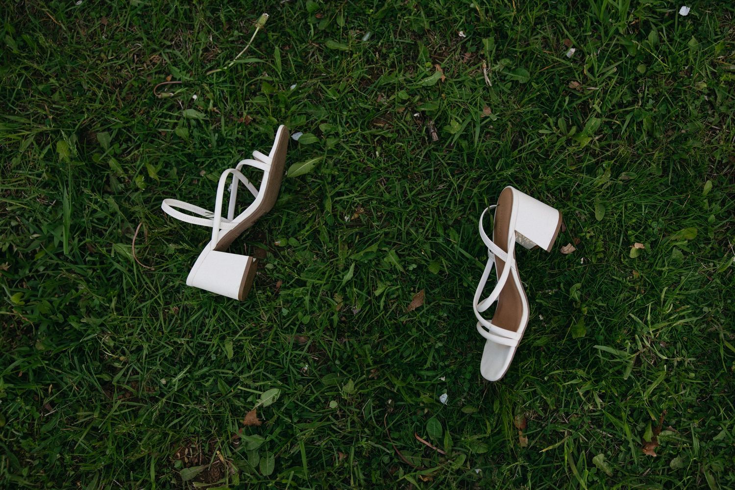 White strappy block heel sandals placed on lush green grass outdoors.