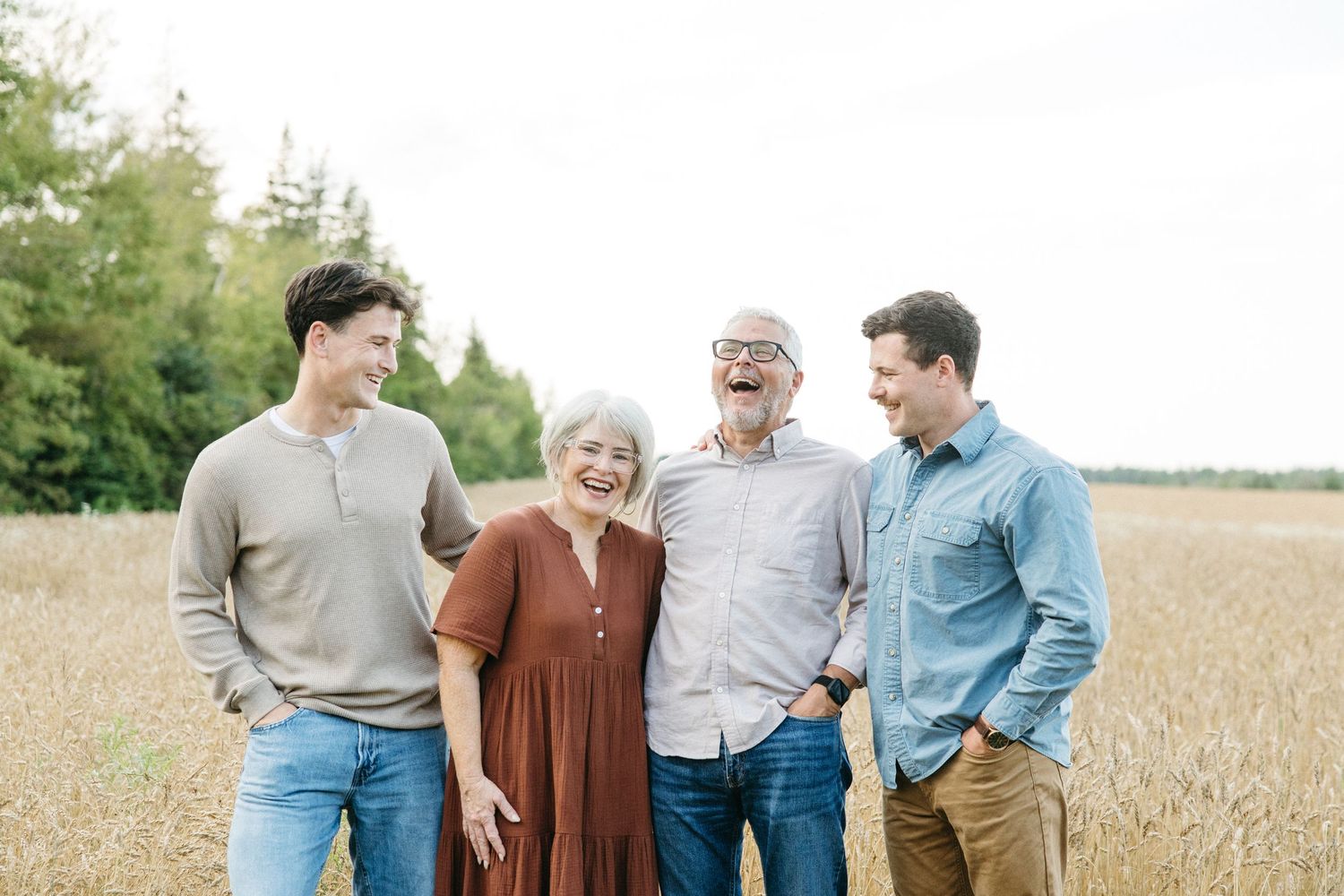 Happy family of four laughing together in a golden wheat field, enjoying a warm outdoor portrait session.