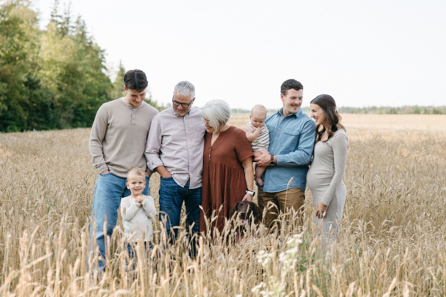 Multi-generational family smiling together in a golden wheat field during an outdoor fall photo session.