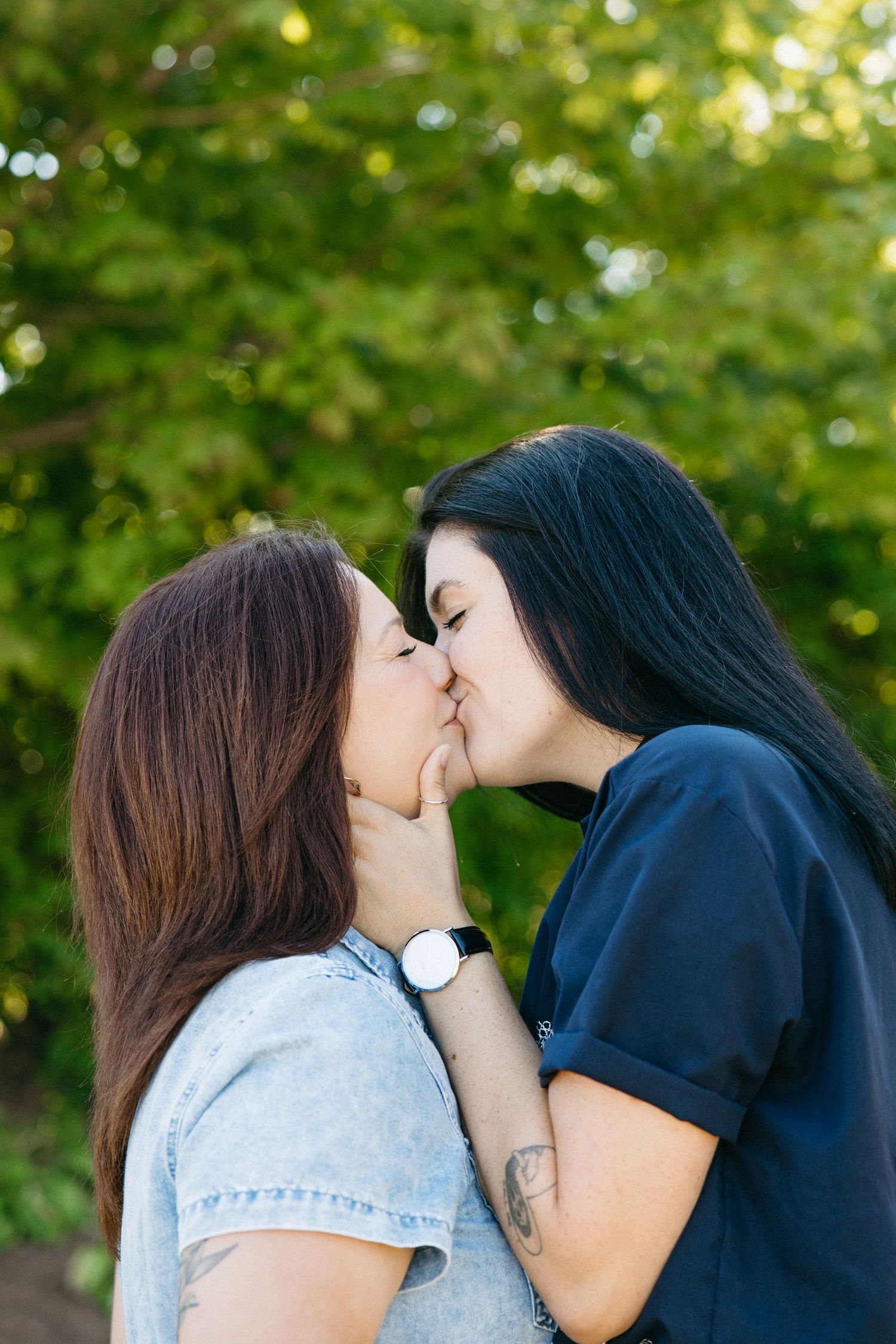 Two people sharing a romantic kiss outdoors with green foliage in the background.