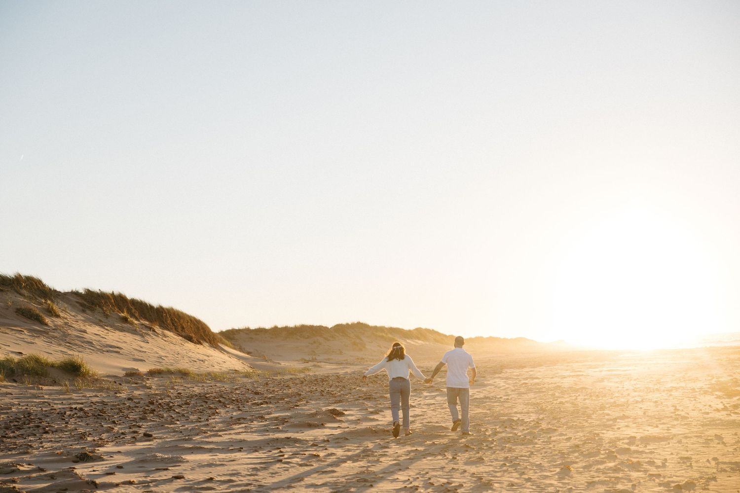 Two people walking together along sandy dunes during golden hour.
