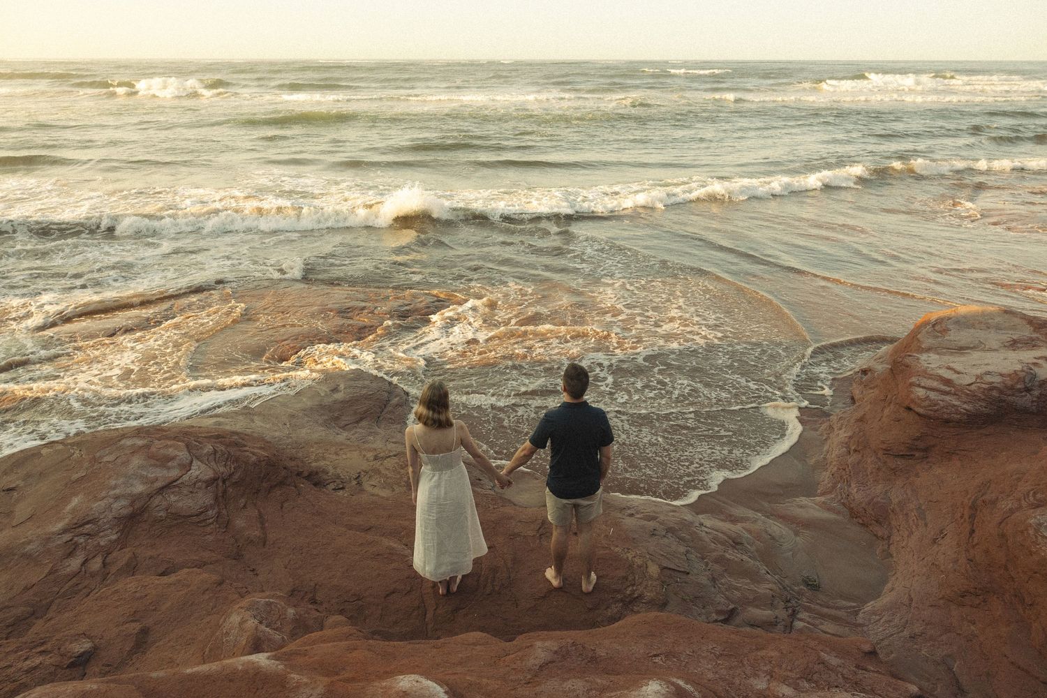 Coastal landscape featuring red rock cliffs and crashing waves during golden hour.