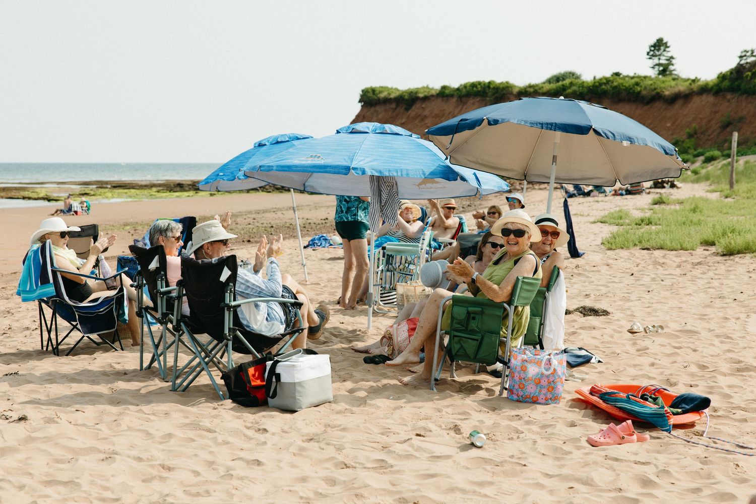 Beach wedding reception setup with blue umbrellas and chairs on sand.