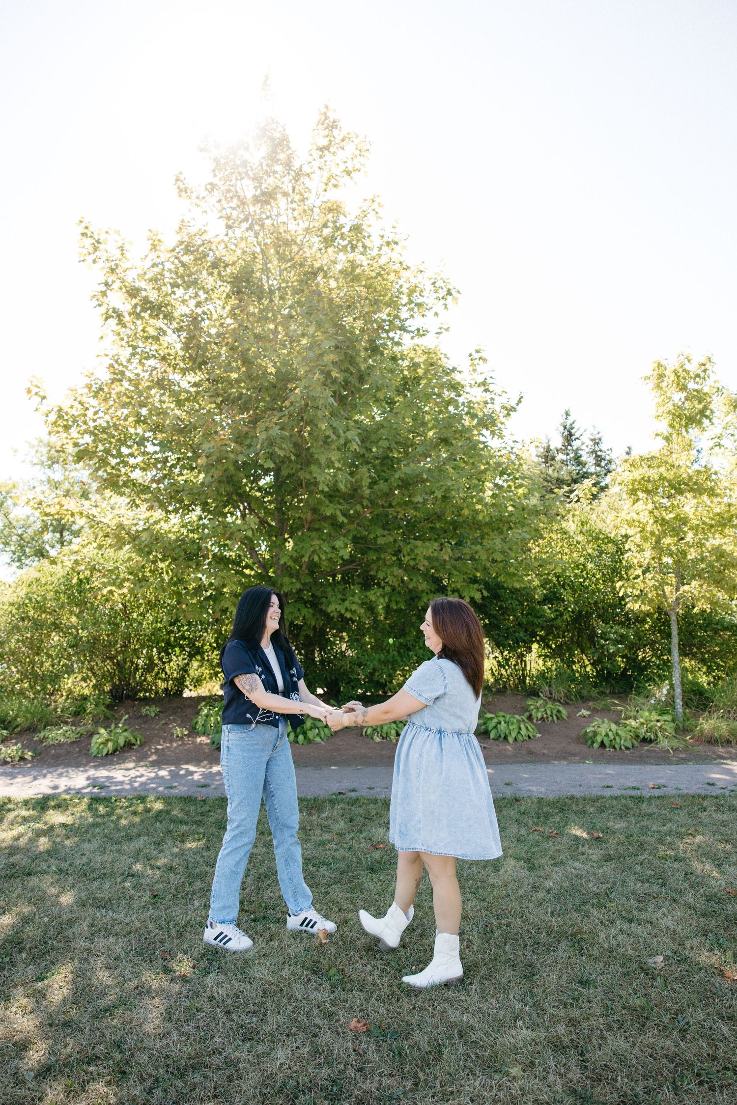 Two people holding hands while standing in a park with lush trees behind them.