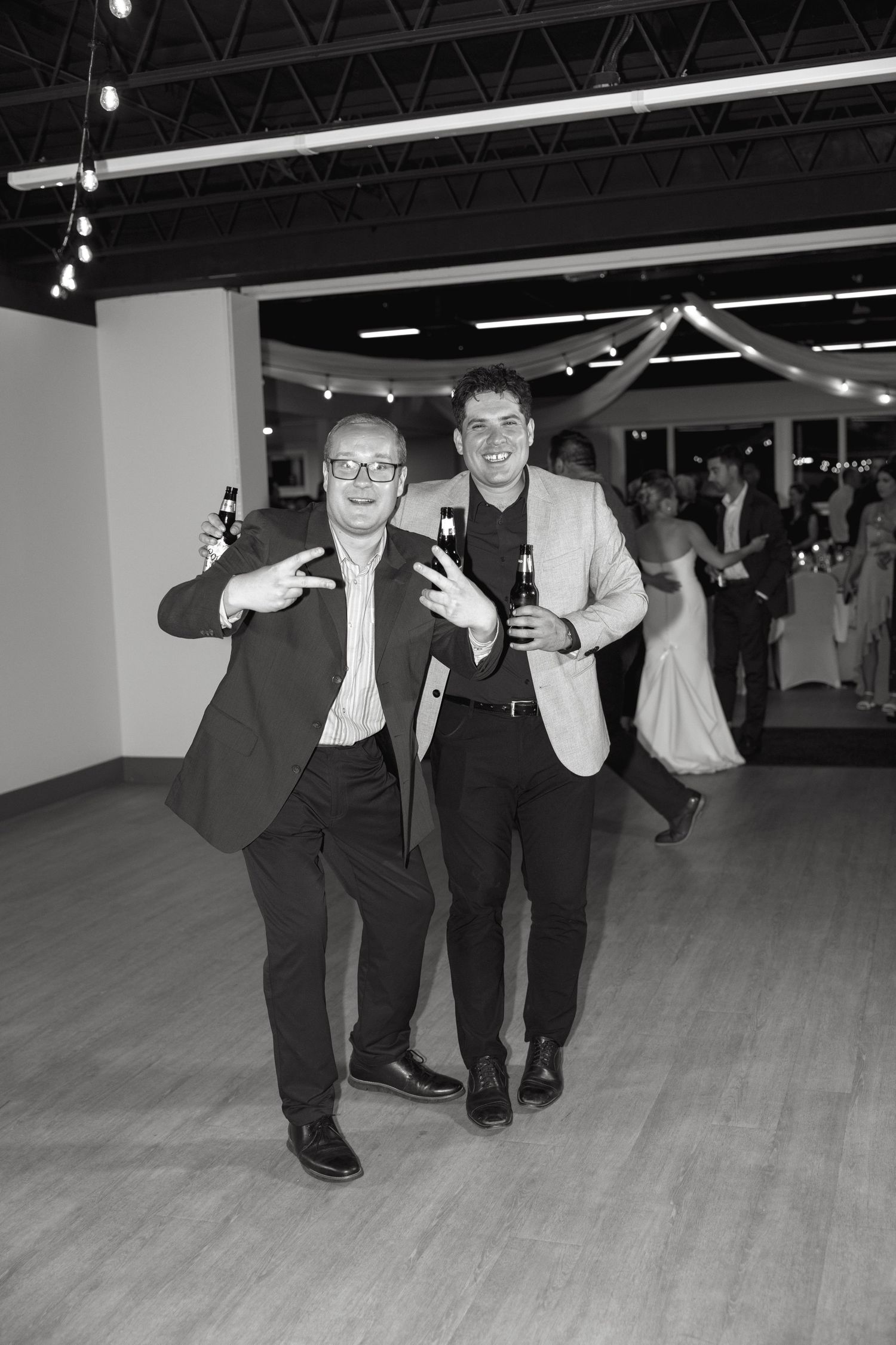 Two men in suits dancing and having fun at wedding reception in black and white.