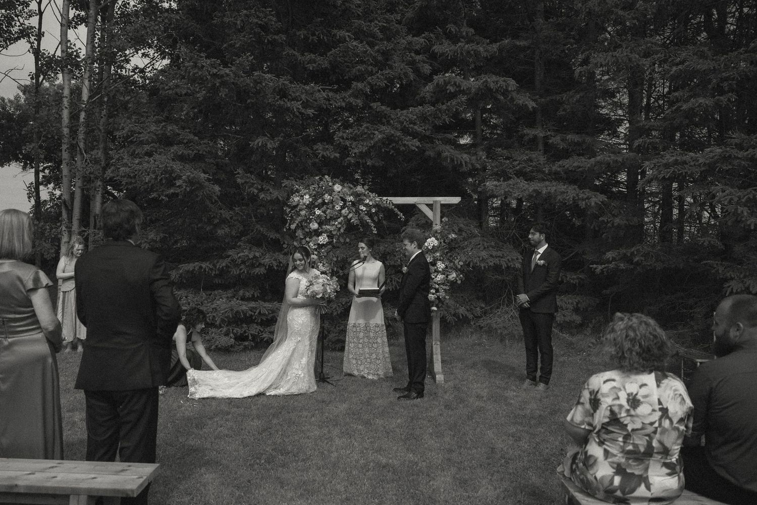 Wedding ceremony progression captured in black and white showing moments under floral arch.