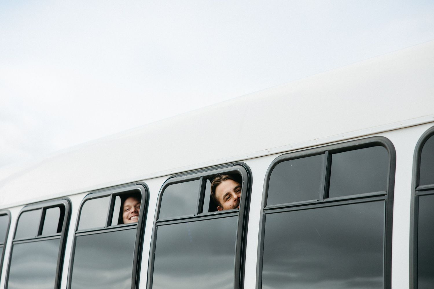 Wedding party members peek out from windows of a vintage bus.