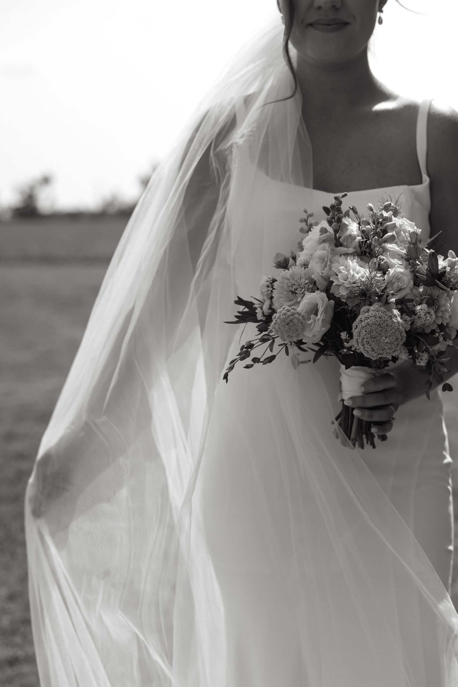 Elegant bridal details featuring white dress and floral bouquet in black and white.