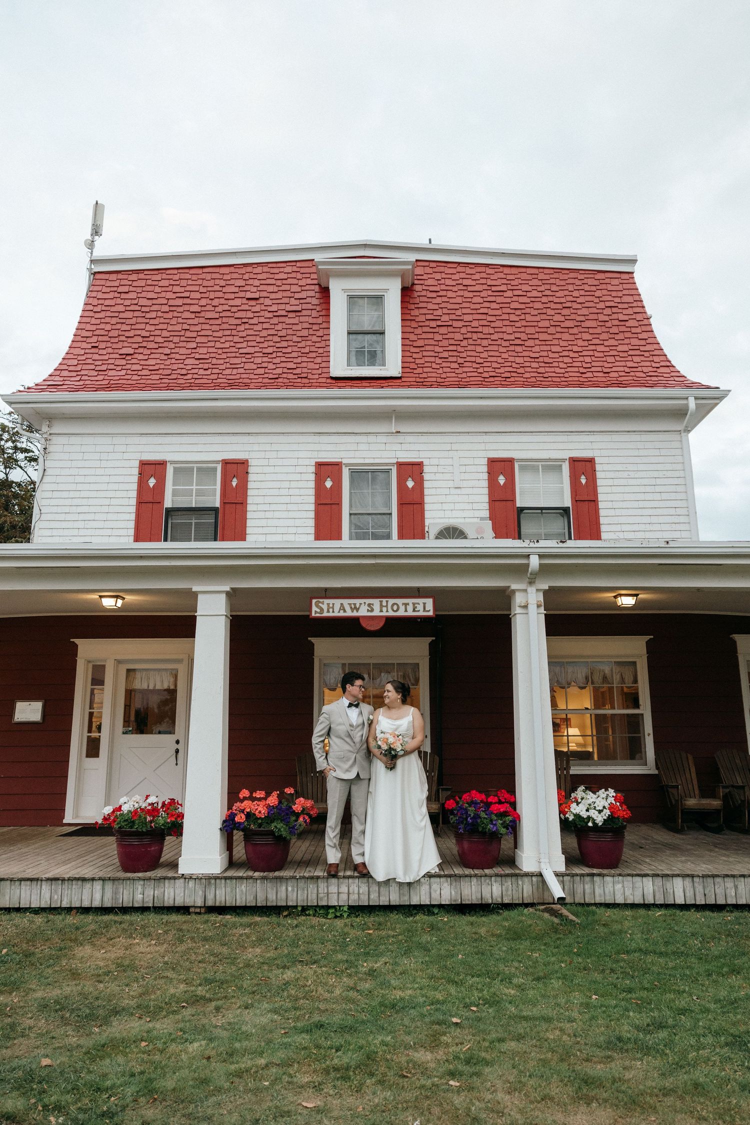 Bride and groom posing on porch of Shaw's Hotel with red roof and colorful flowers.