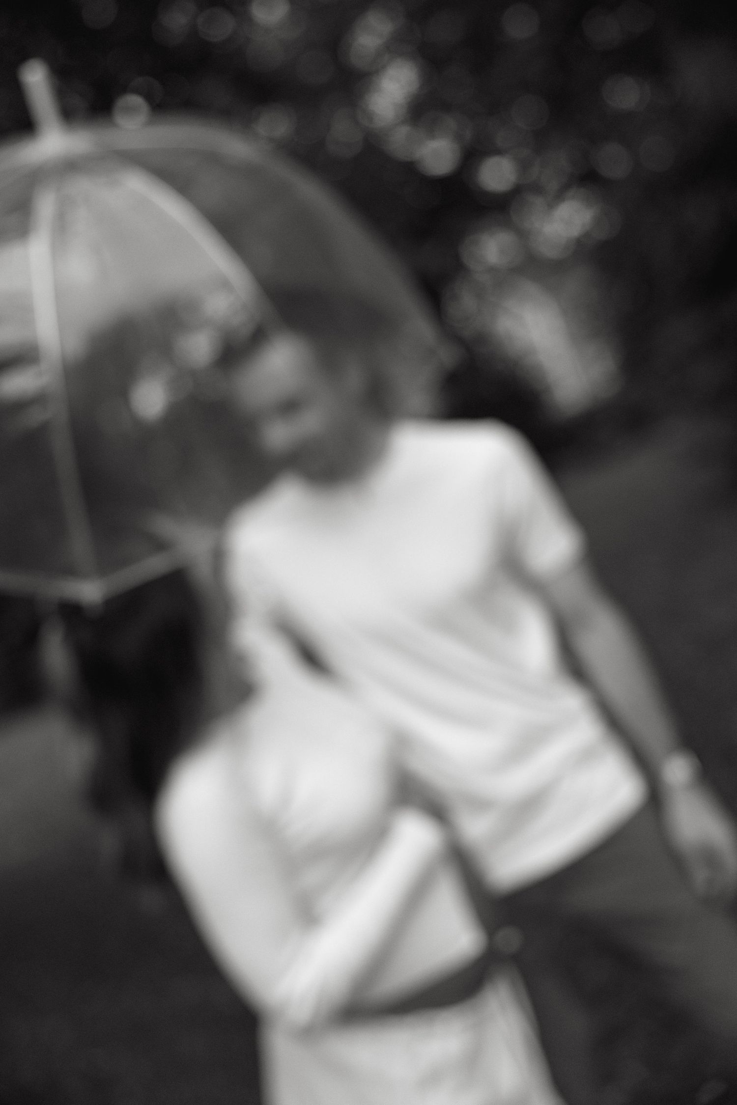 Blurry black and white photo of a couple sharing a romantic moment under a clear dome umbrella outdoors.