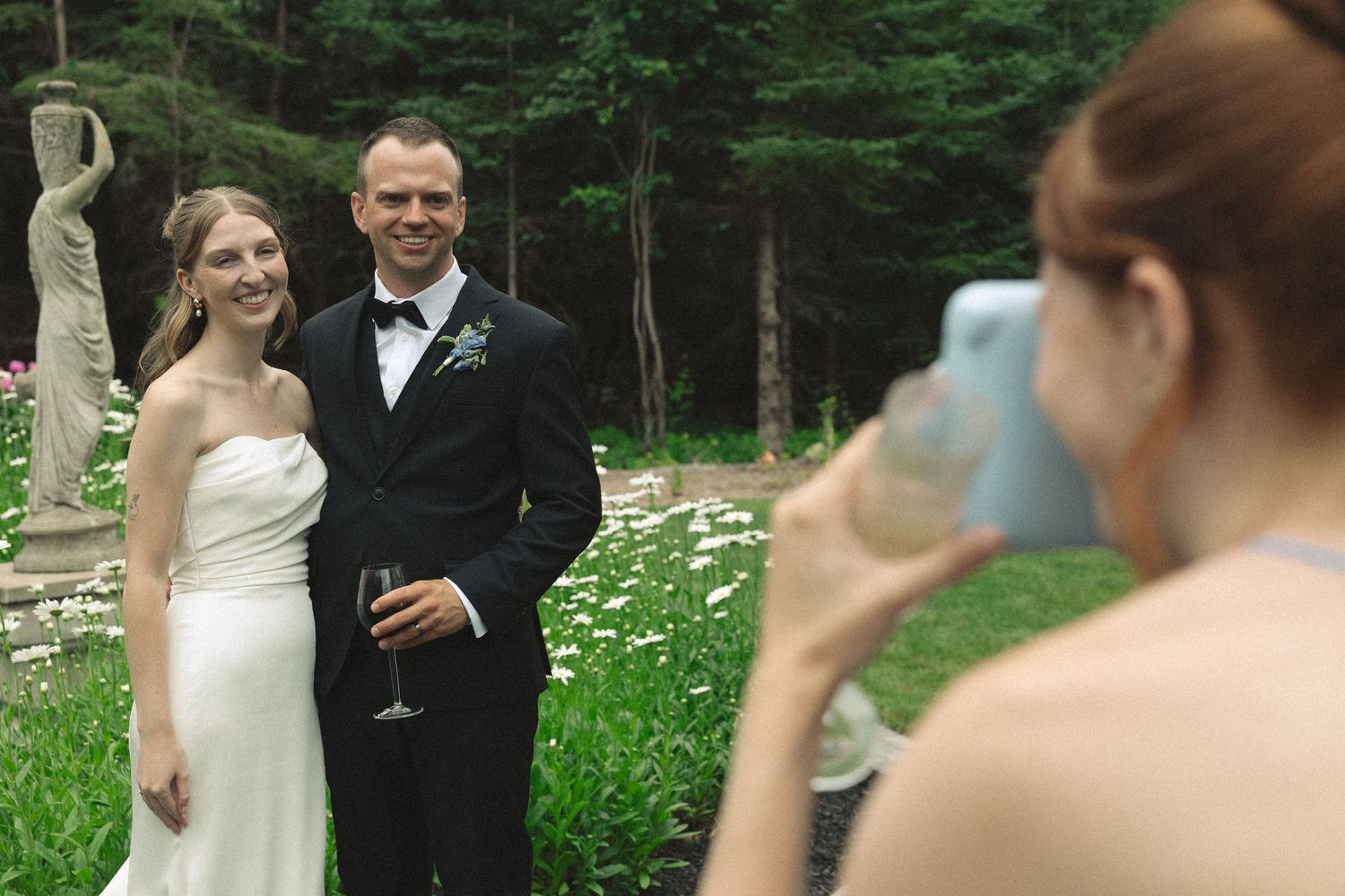 Wedding guest photographs smiling bride and groom with a smartphone at their reception.