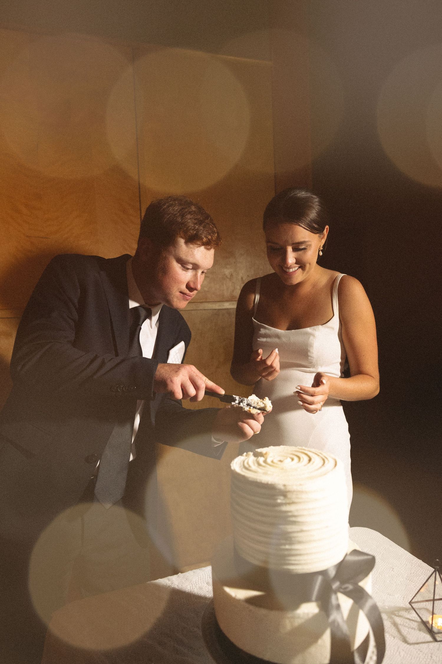 A couple in wedding attire shares a playful moment while cutting their white wedding cake together.