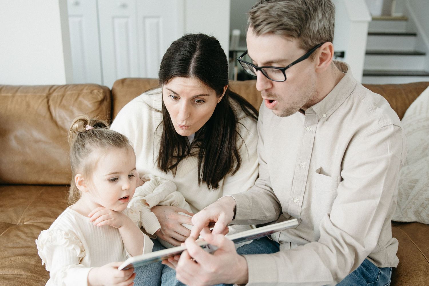 A family gathers on their leather couch to look at a tablet device together.