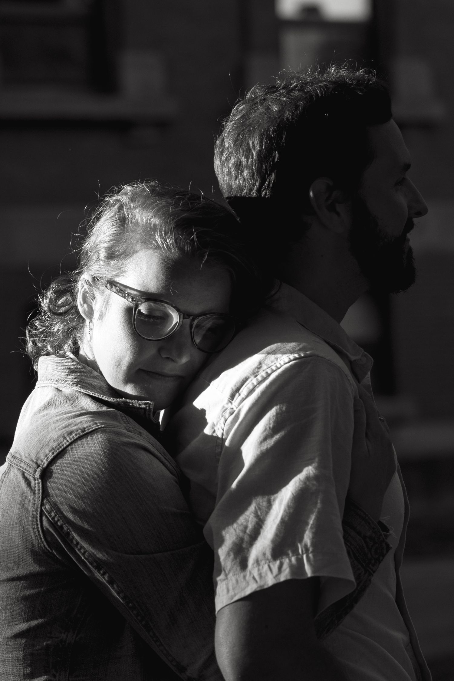 A tender black and white portrait of a couple embracing against a dark background.