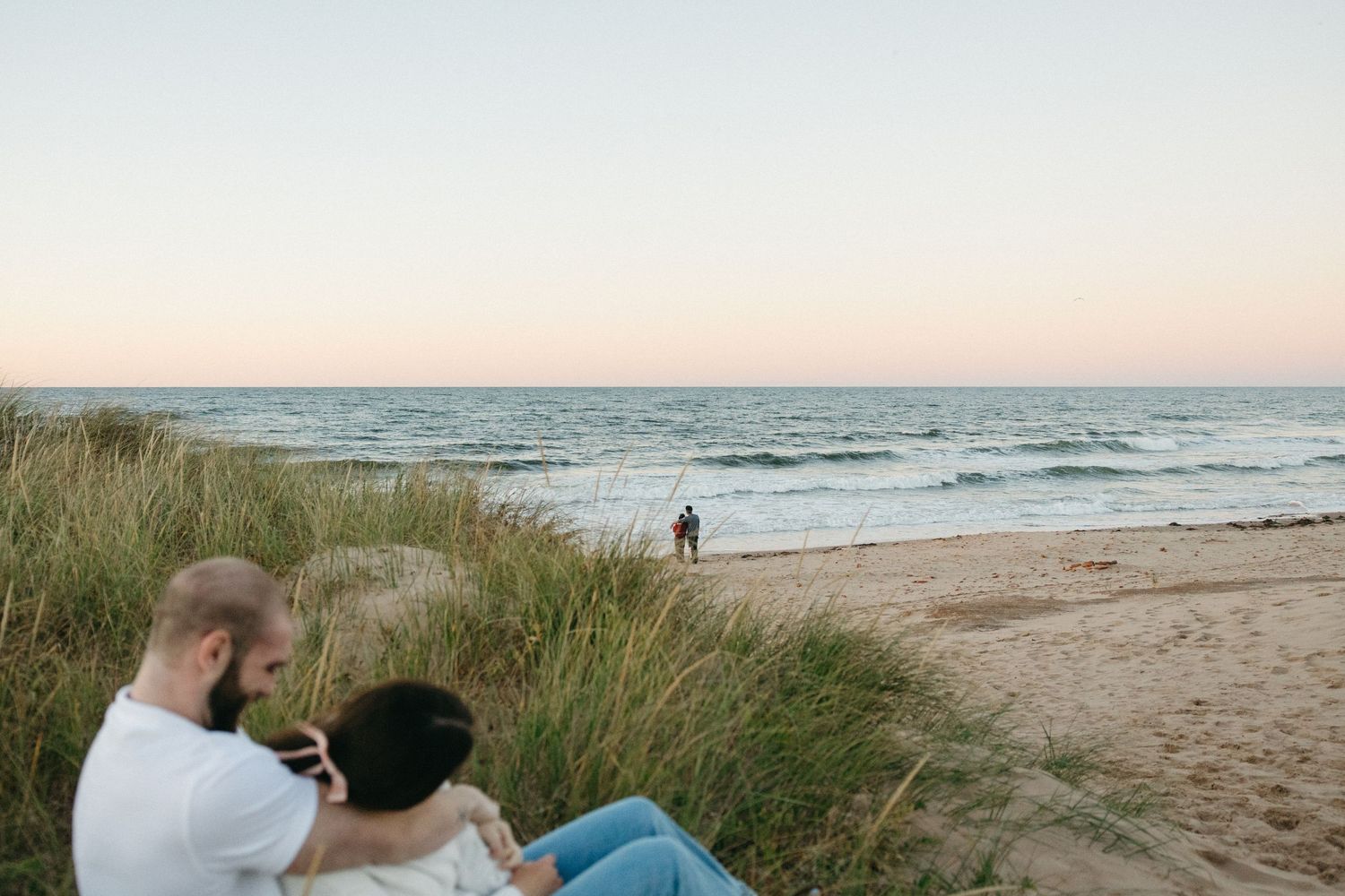 Scenic beach landscape with dunes, ocean waves, and setting sun.