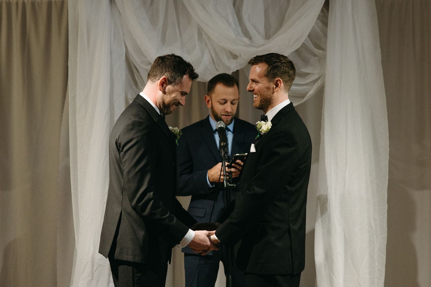 Wedding ceremony taking place under white draped backdrop with officiant and couple.