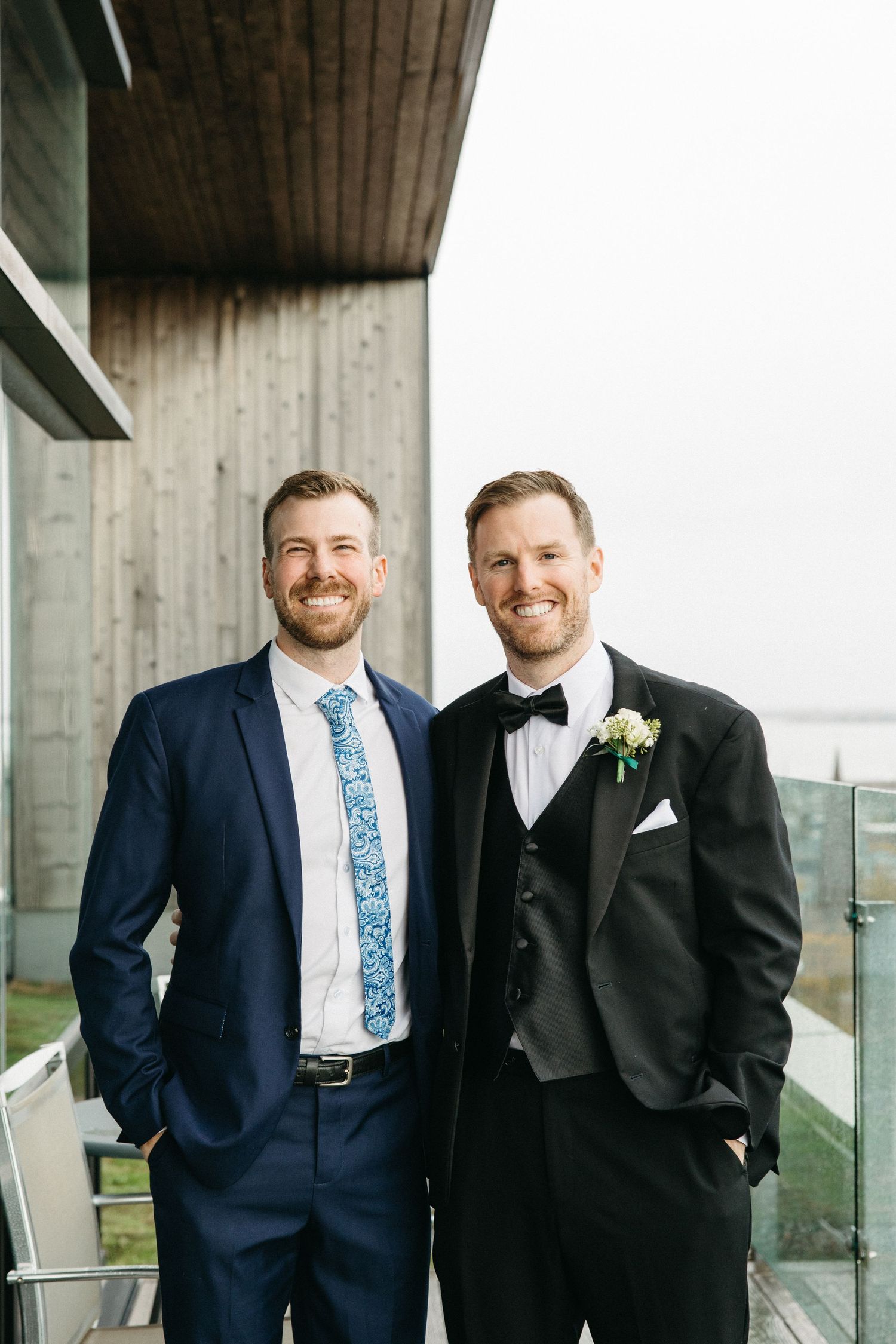 Two people in formal suits share a joyful moment on an outdoor terrace.
