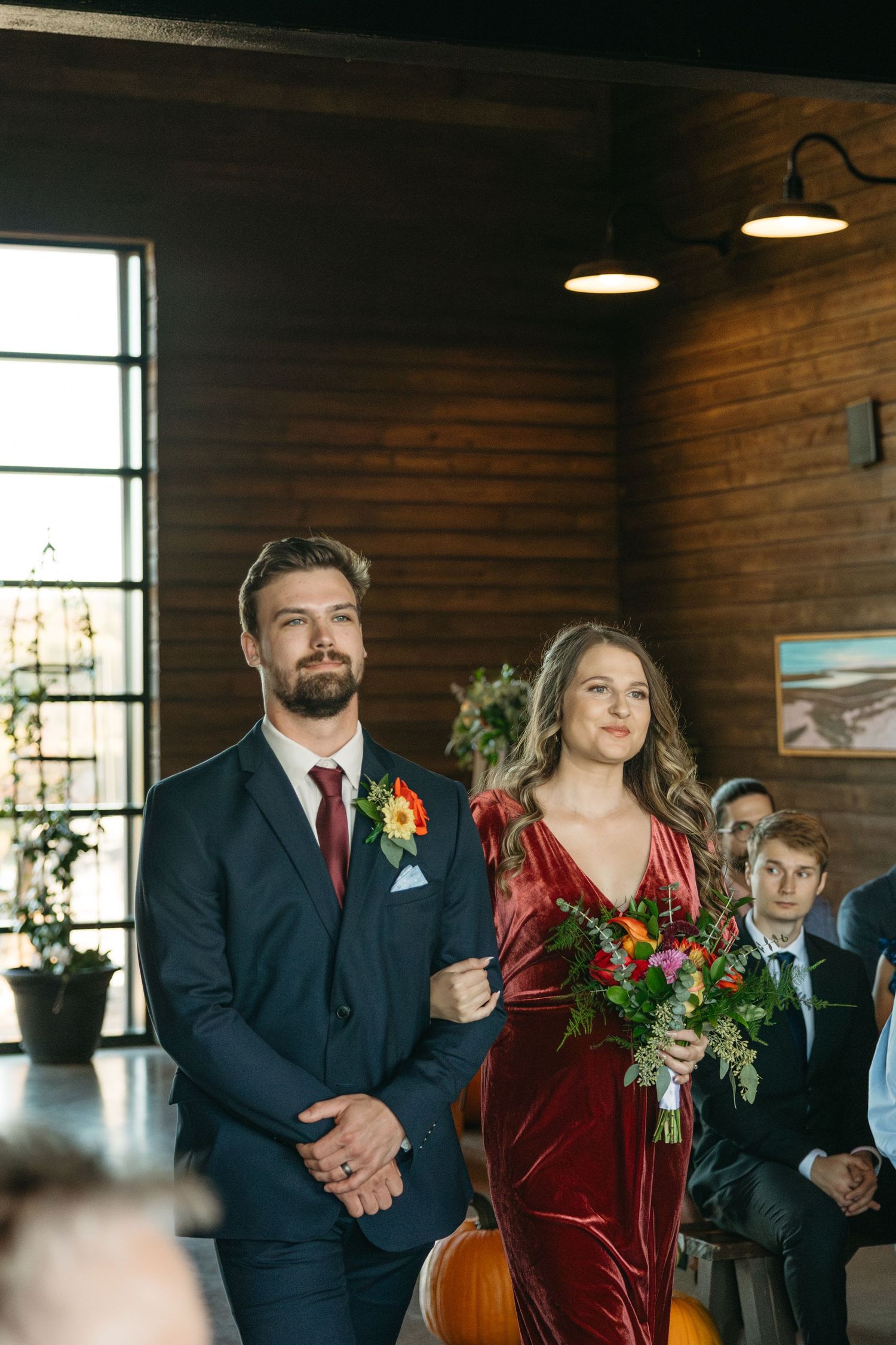 Wedding party members in formal attire standing together in rustic brick venue with natural lighting.