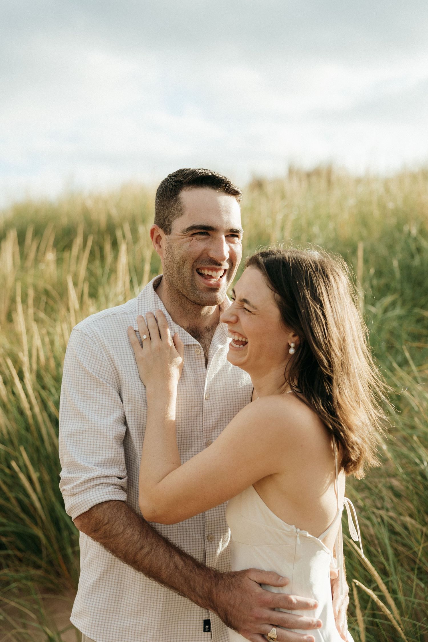 A couple shares joyful laughter and embraces in a sun-lit field of tall grass.