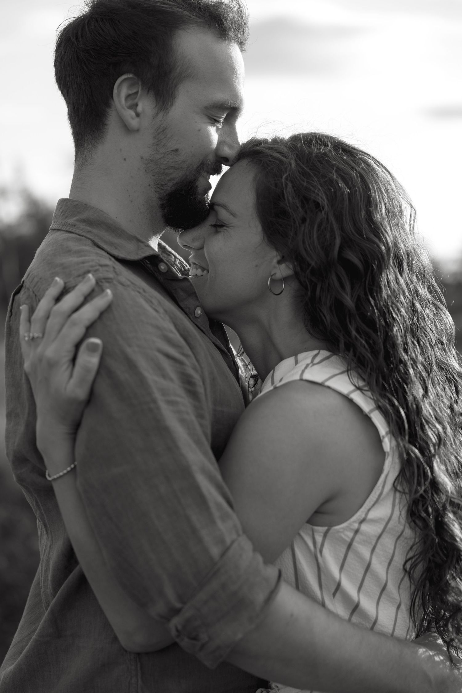 Black and white photo of a romantic couple embracing and about to kiss outdoors at sunset.