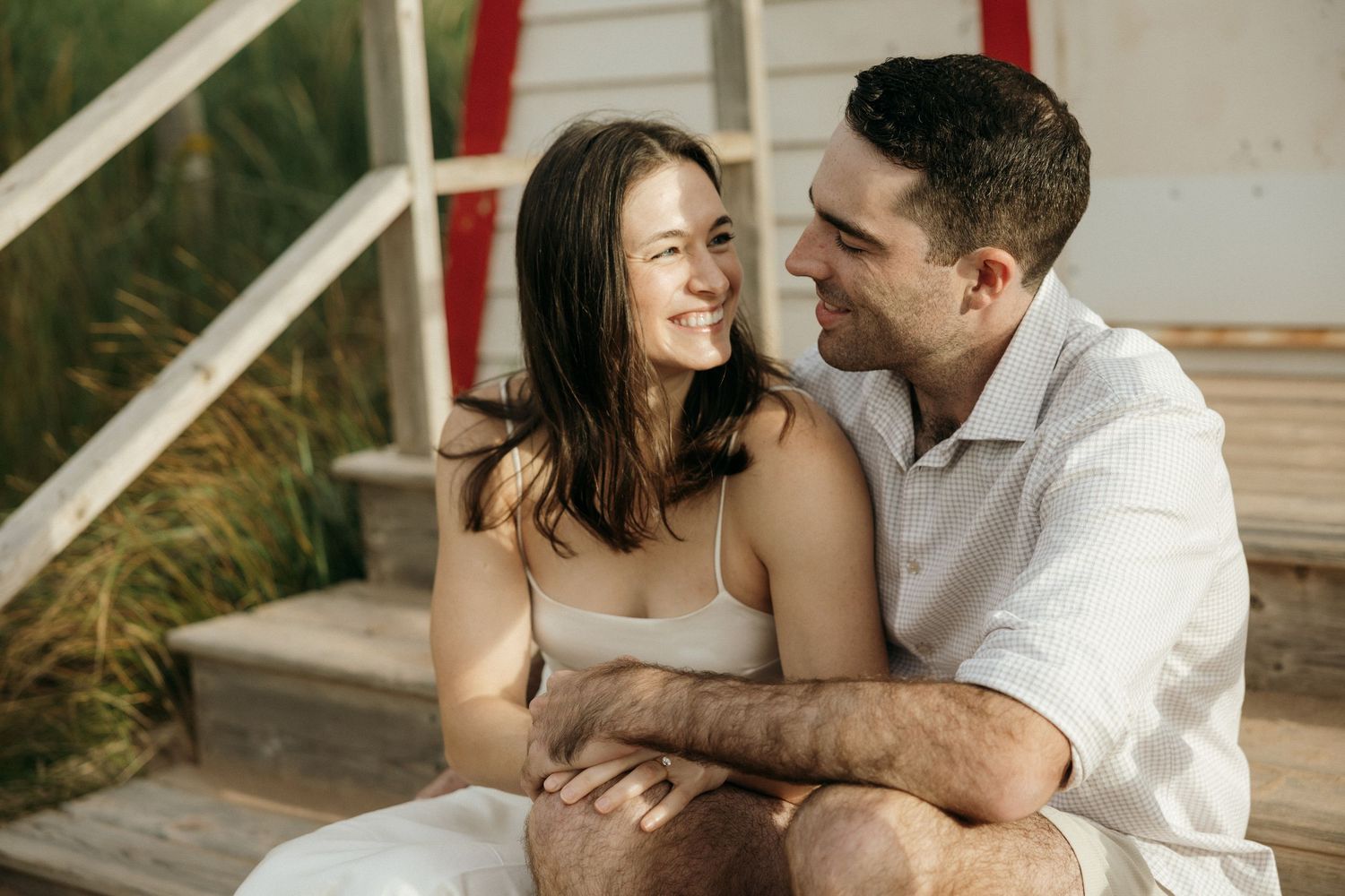 A couple shares tender moments while sitting together by a white lighthouse.