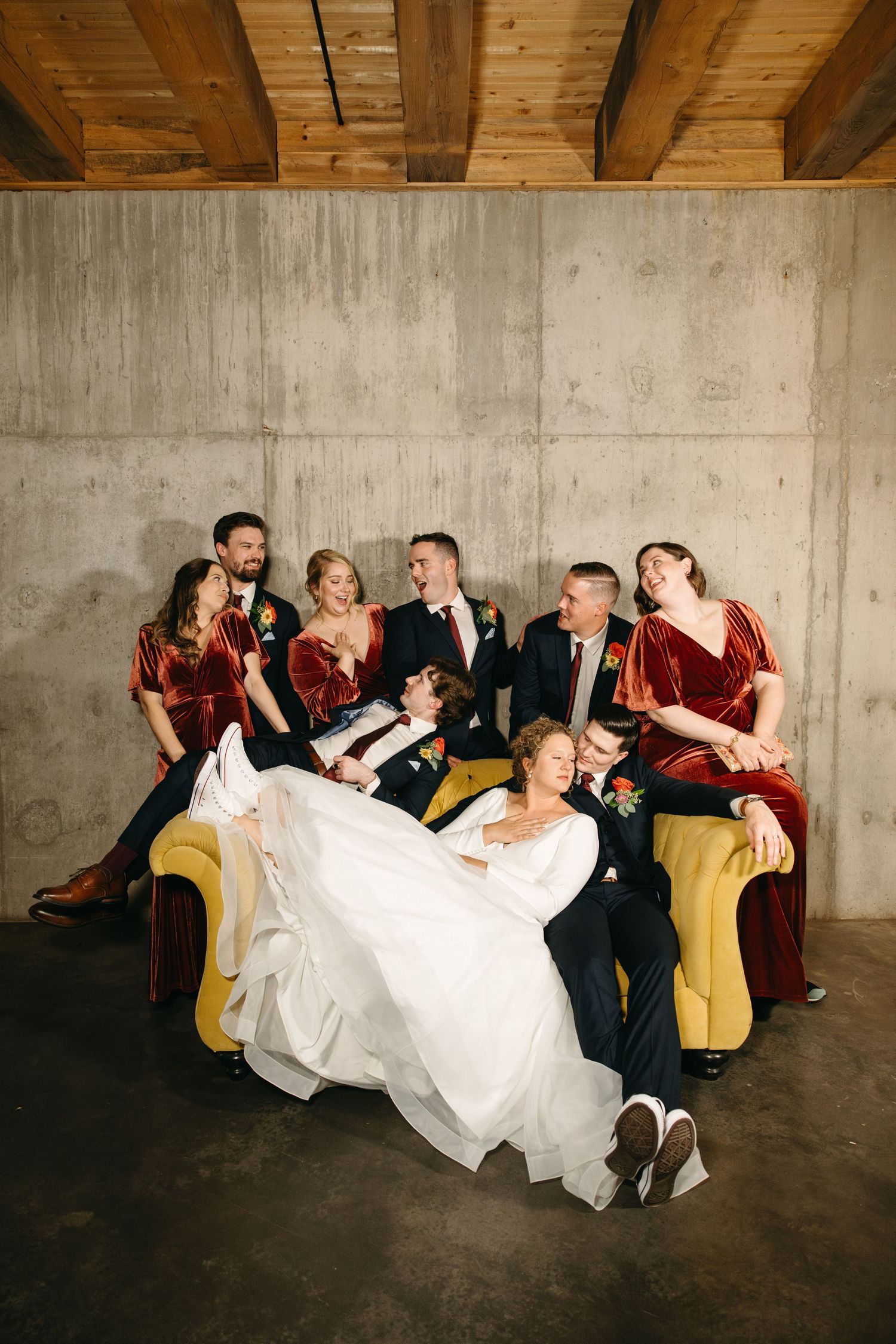 Wedding party lounges on a yellow couch against concrete wall in stylish photo series.