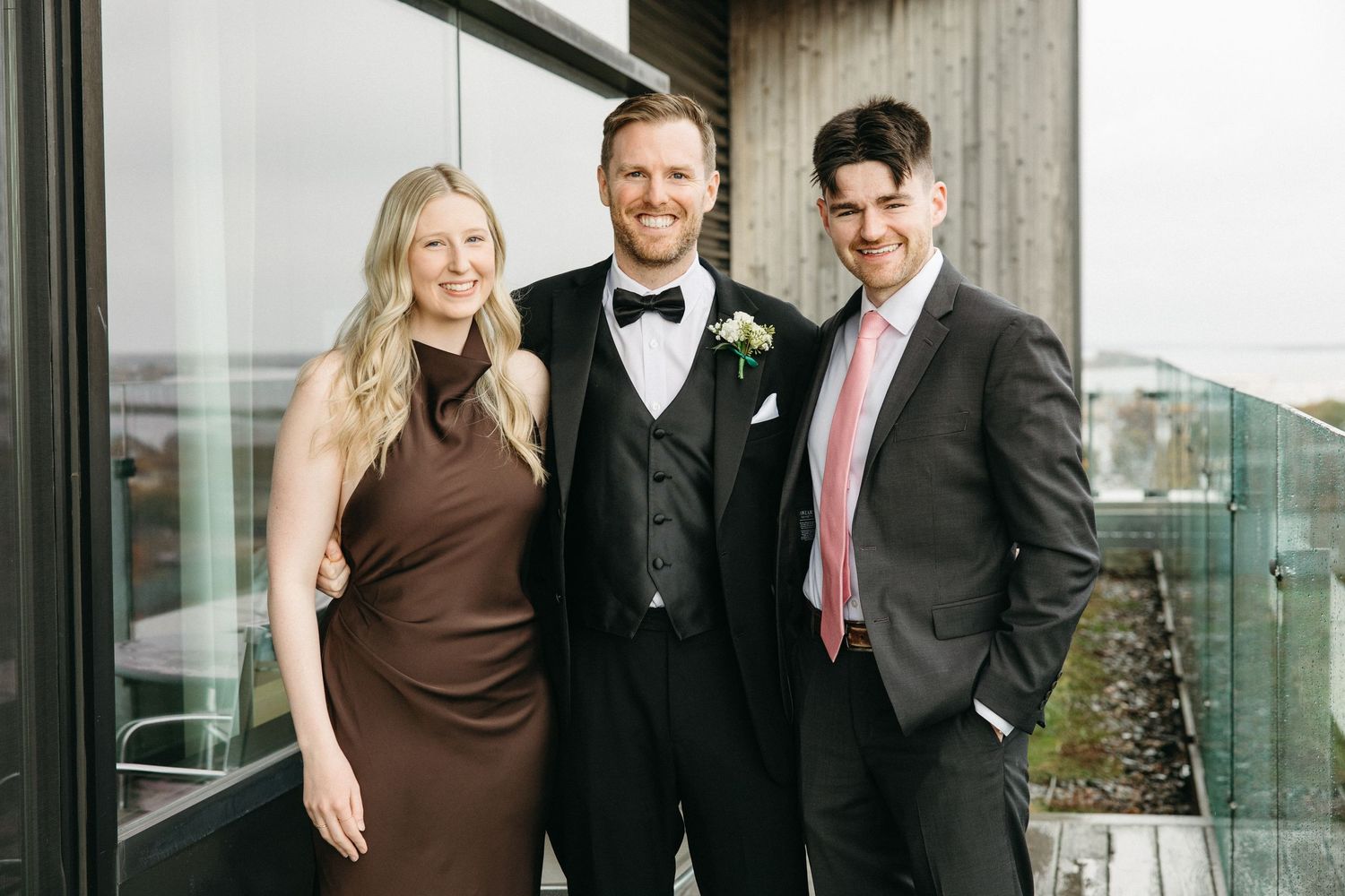 A group in formal attire poses on a modern balcony with city views.