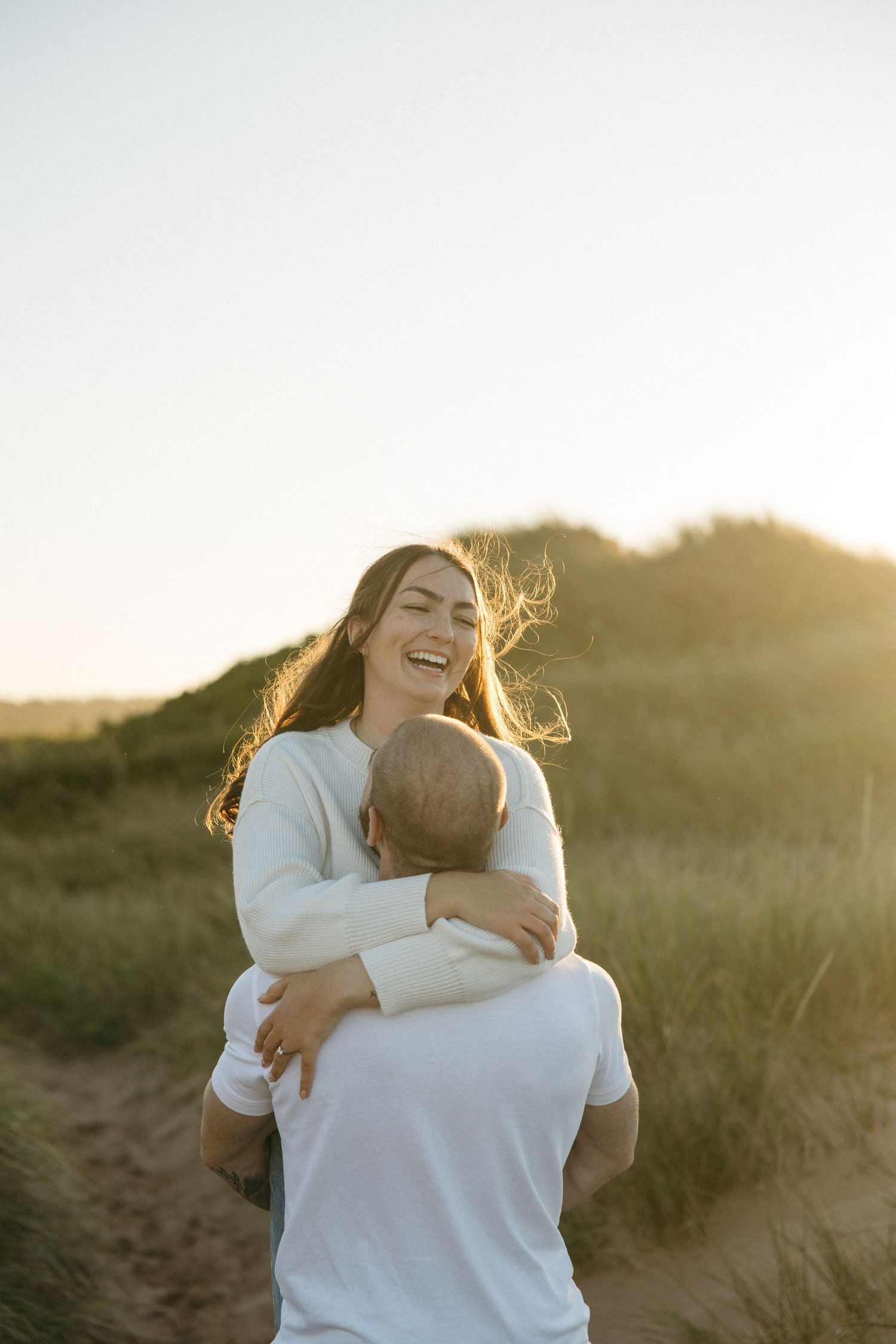 A couple embraces warmly against a sunset backdrop in a natural outdoor setting.