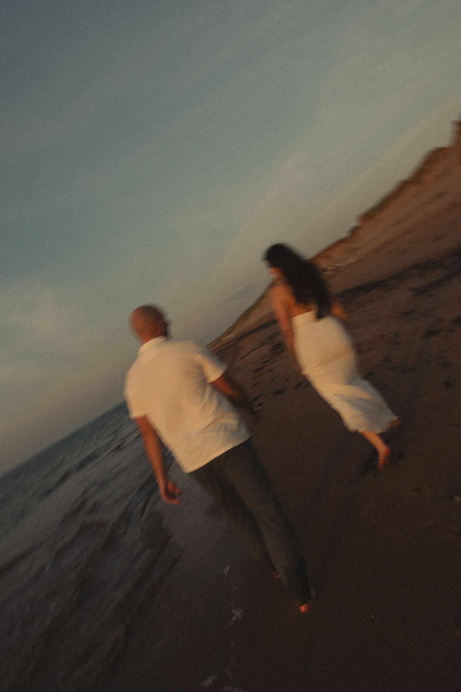Couple walking hand in hand along a sandy beach at sunset, motion blur capturing romantic movement.
