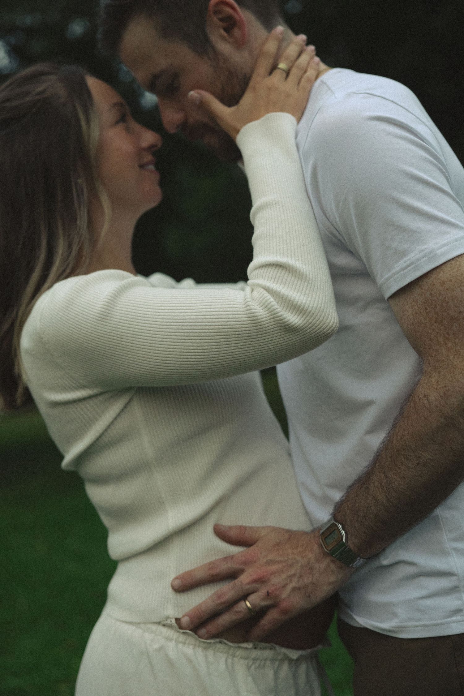Romantic couple sharing tender moment outdoors, woman in white sweater touching mans face affectionately.