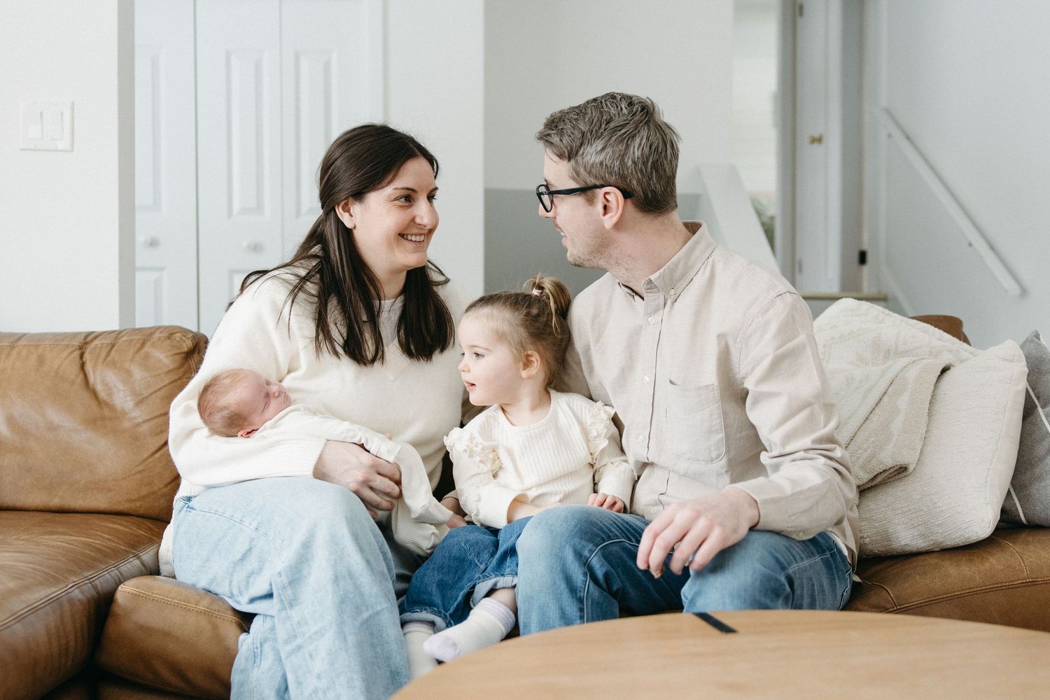 A family relaxes together on their living room couch in casual white and denim outfits.