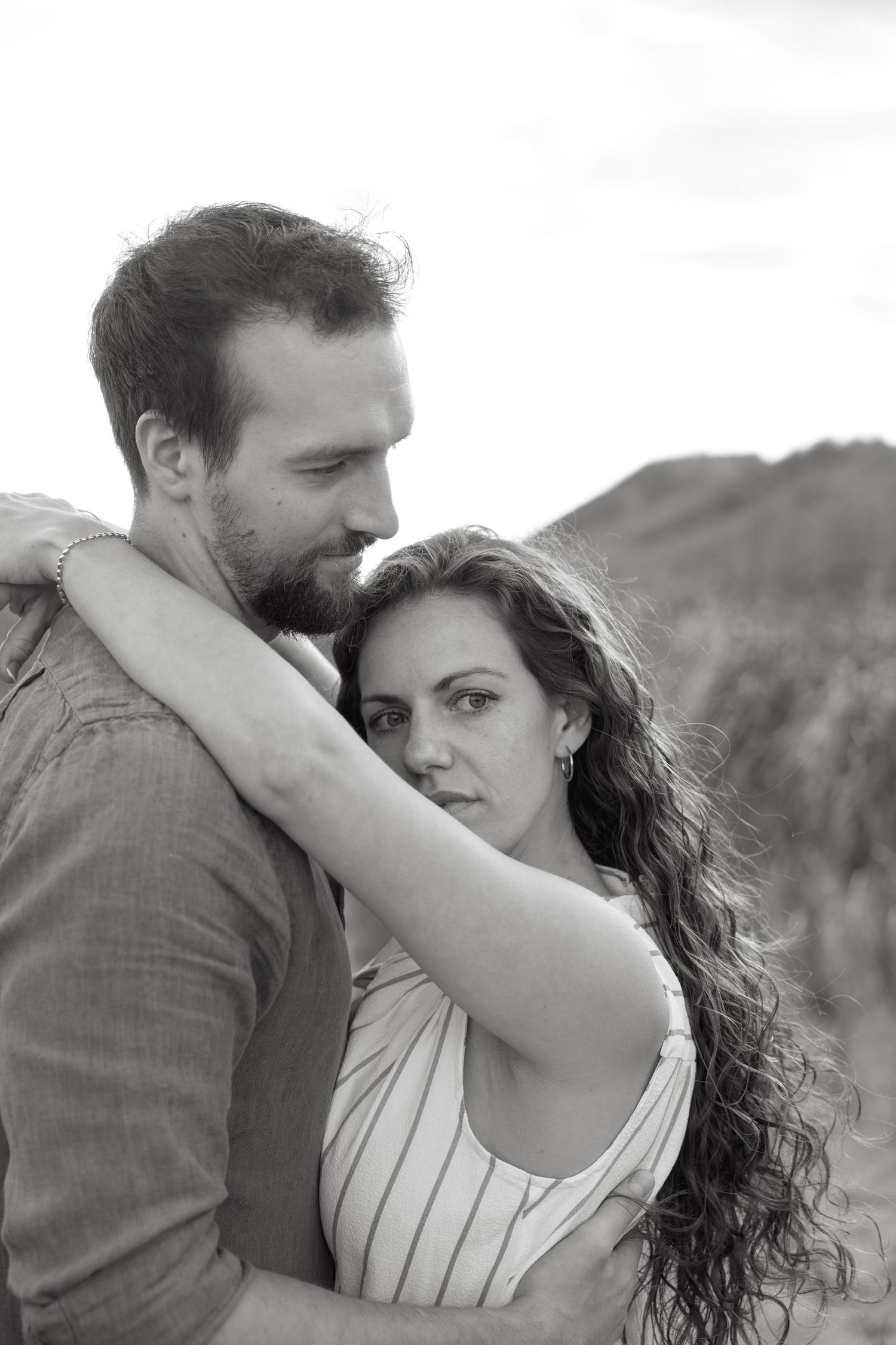 Black and white photo of a couple embracing outdoors, woman with curly hair looking at camera while man gazes down tenderly.