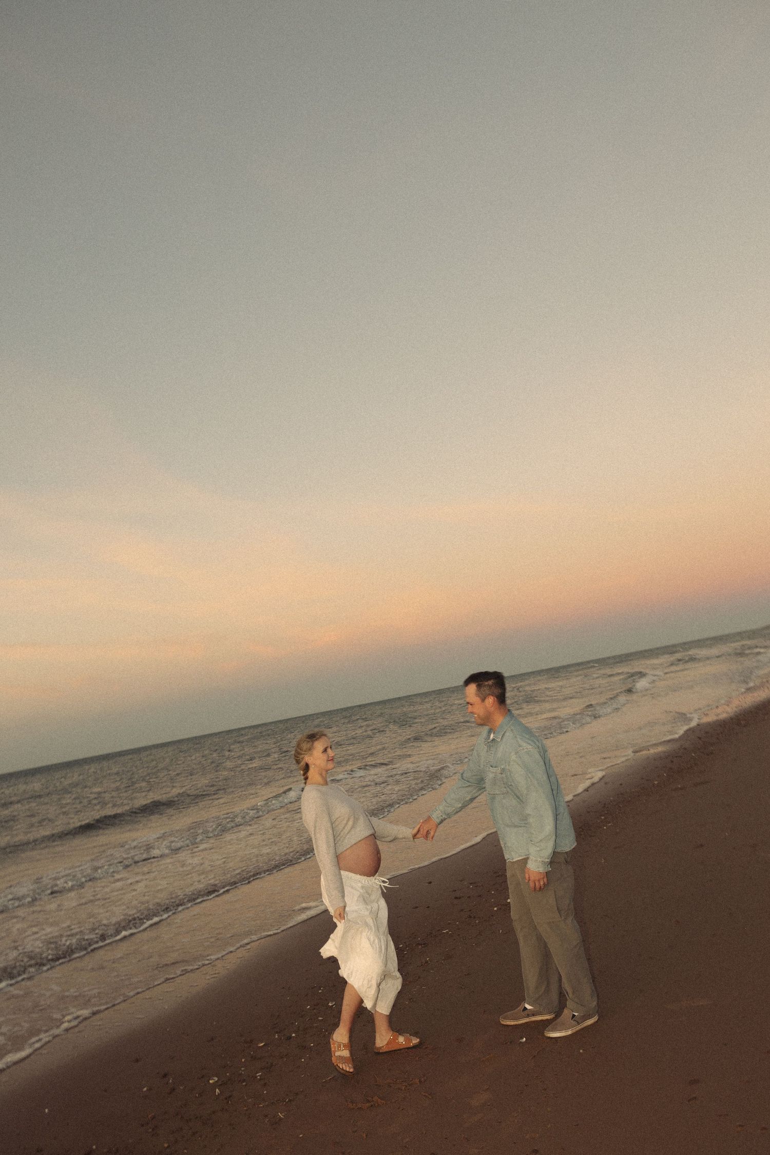 Two people dance together on a beach during golden hour.