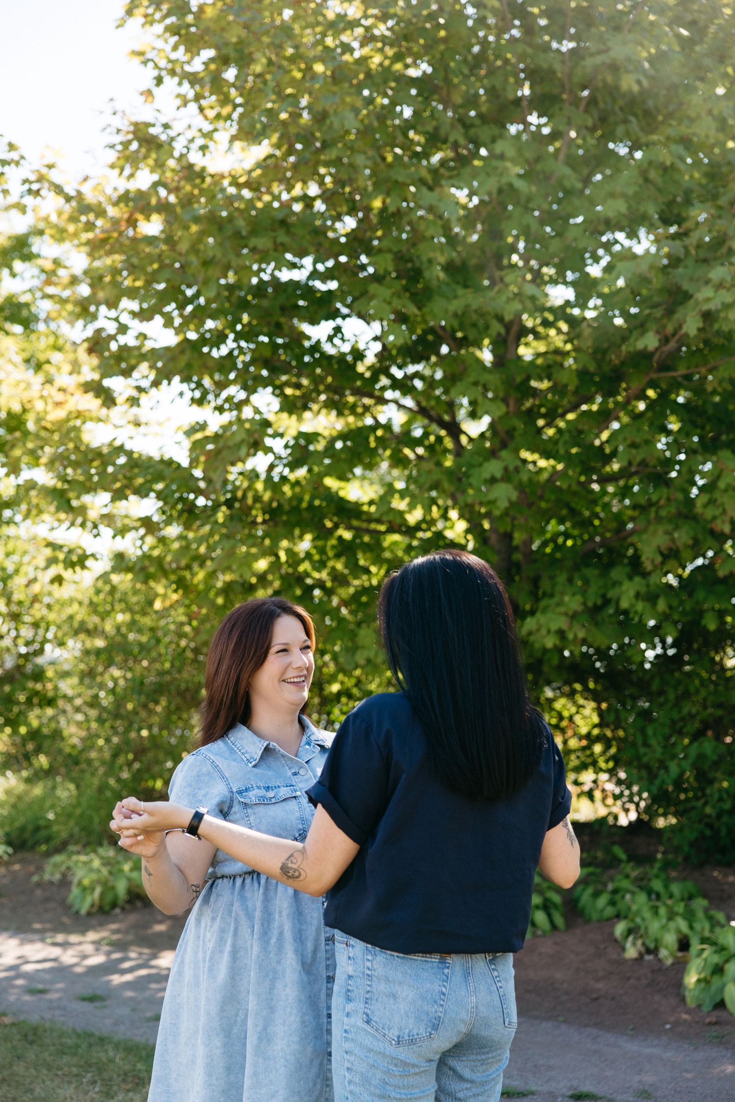 Two friends sharing a joyful moment outdoors with sunlit trees in the background.