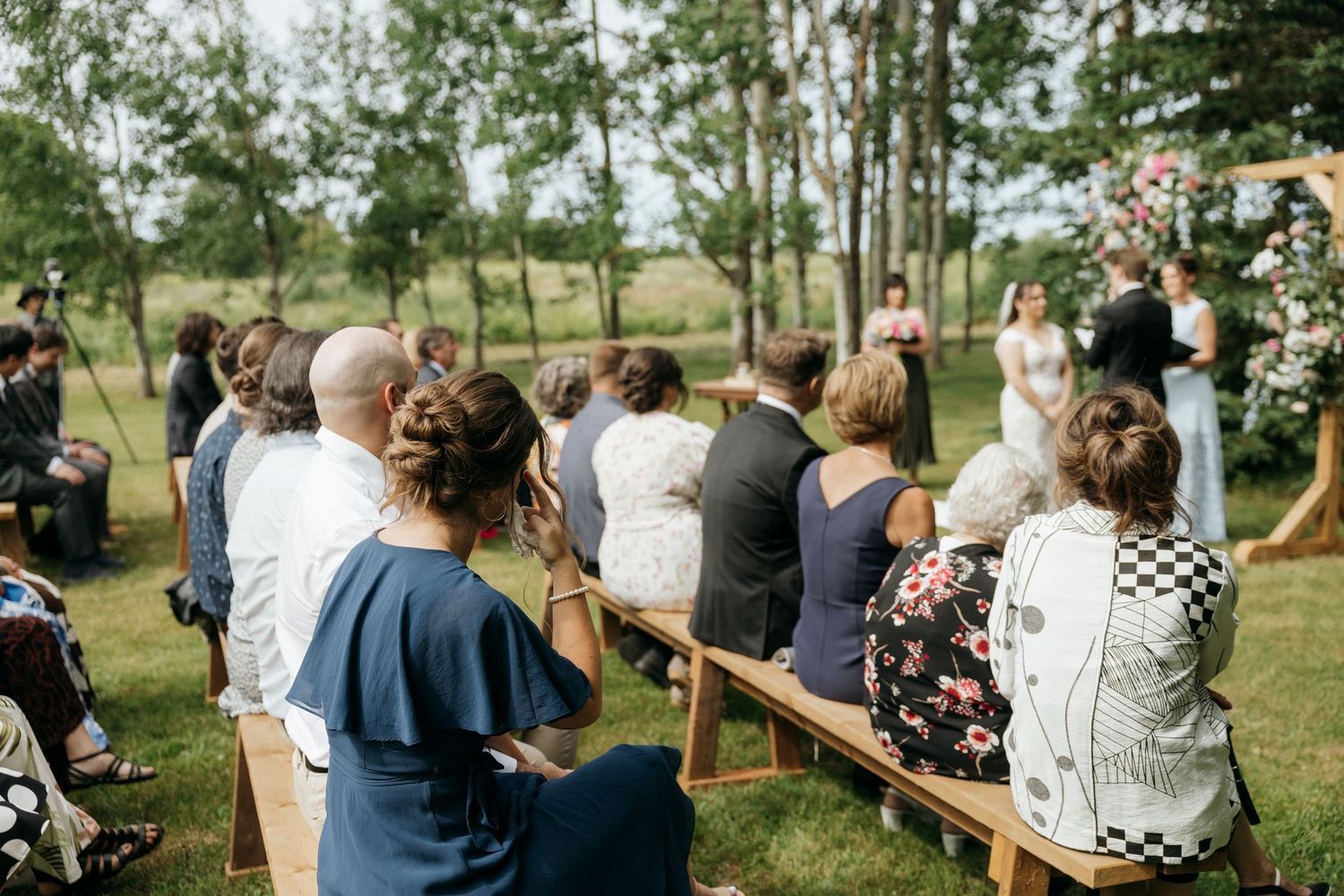 Side view of wedding guests seated on wooden benches during outdoor ceremony.