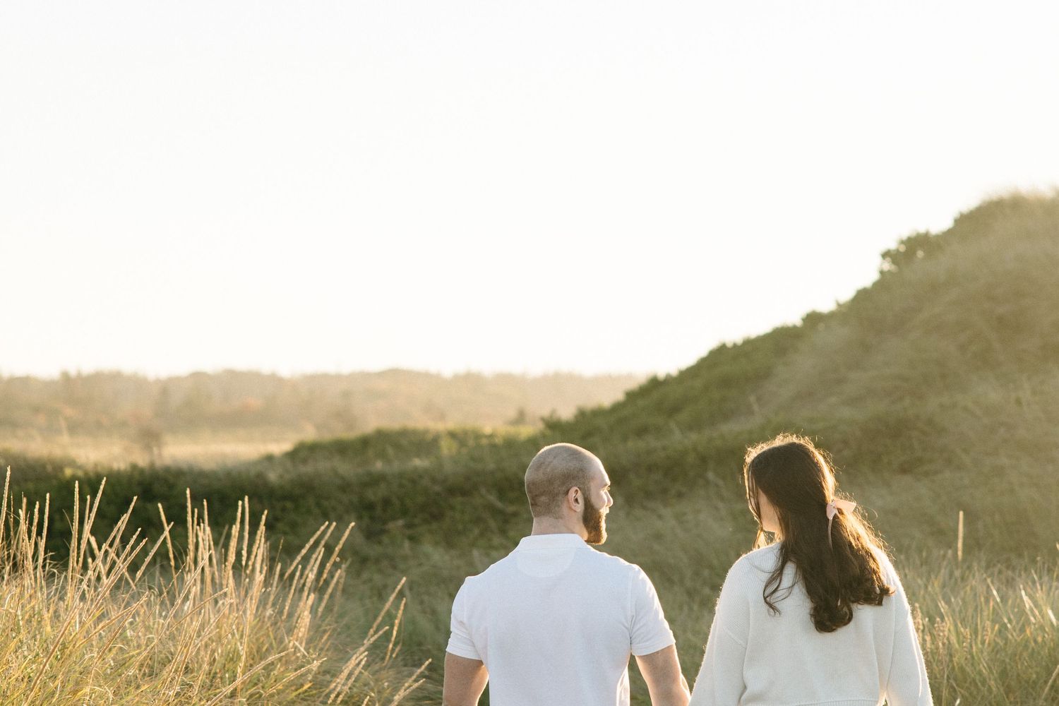 Silhouetted figures walk hand in hand along scenic coastal path at sunset.