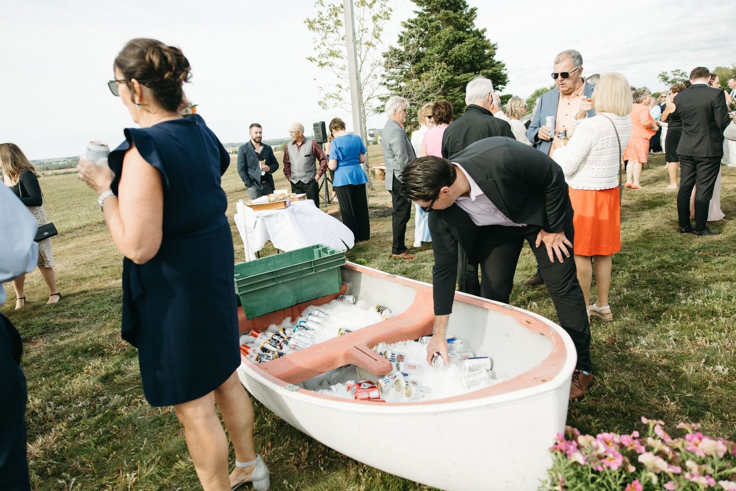 Guests mingling around white tables at an outdoor wedding reception on a grassy hillside.