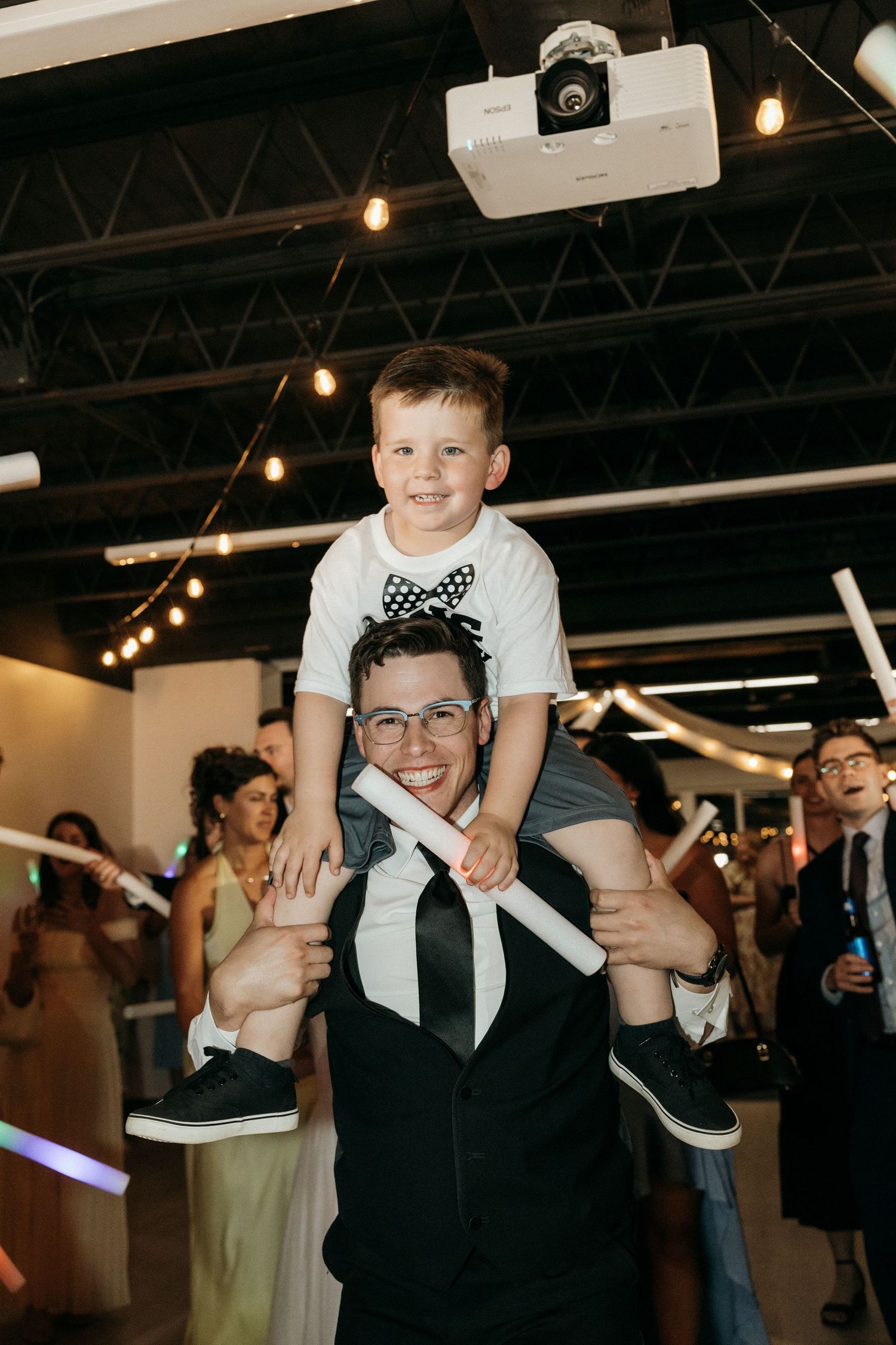 A playful moment at a wedding reception as someone gives a child a shoulder ride on the dance floor.