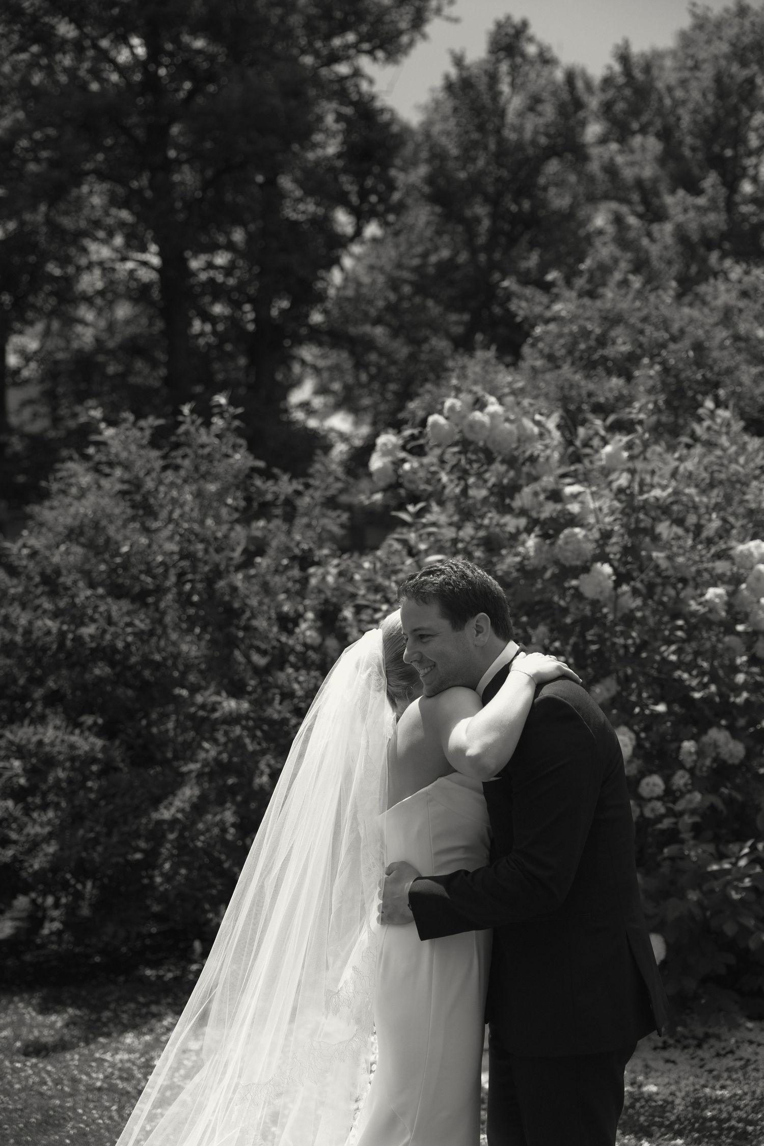 A romantic black and white wedding portrait captured in a blooming garden setting.