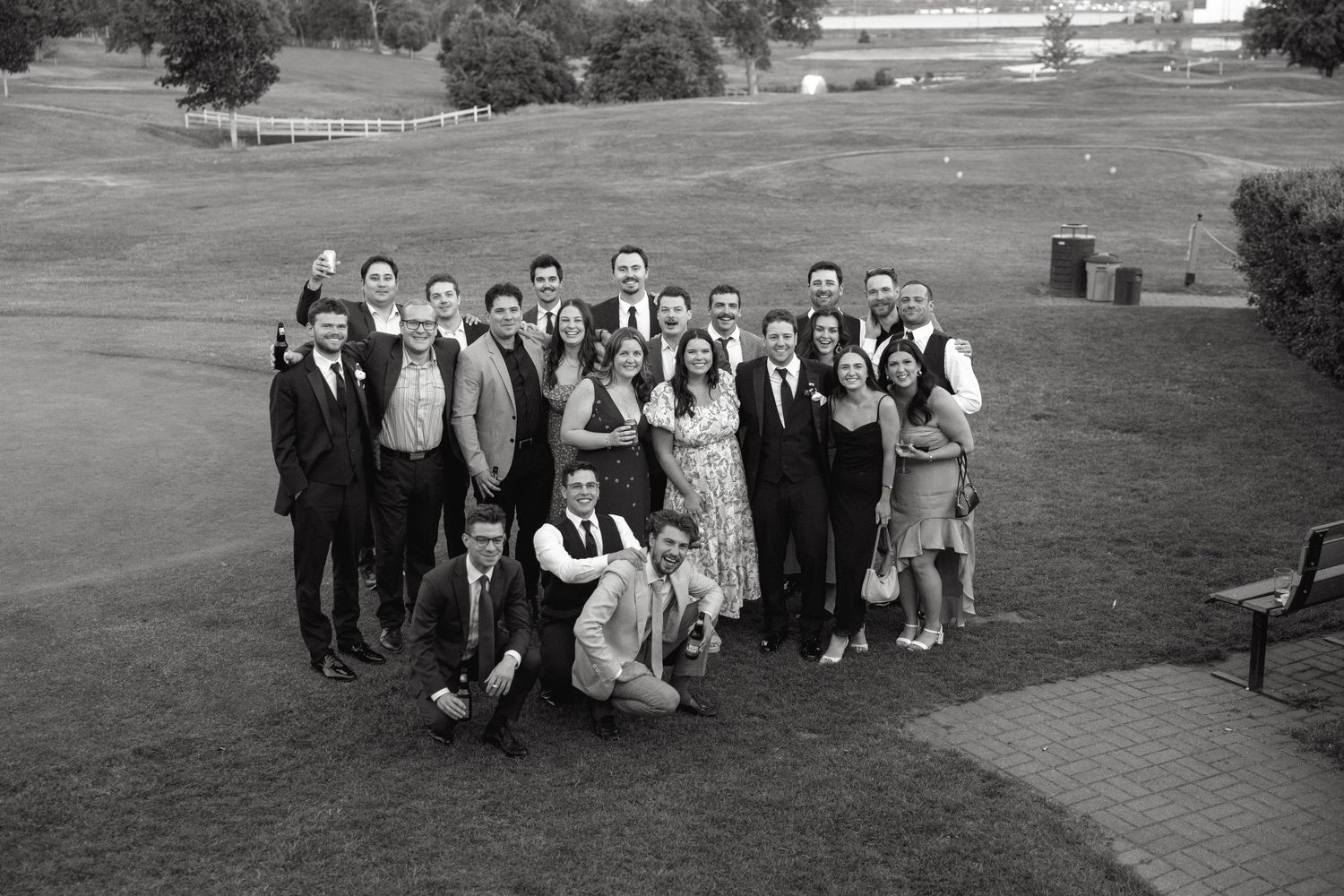 Wedding party poses together on golf course for group photo.
